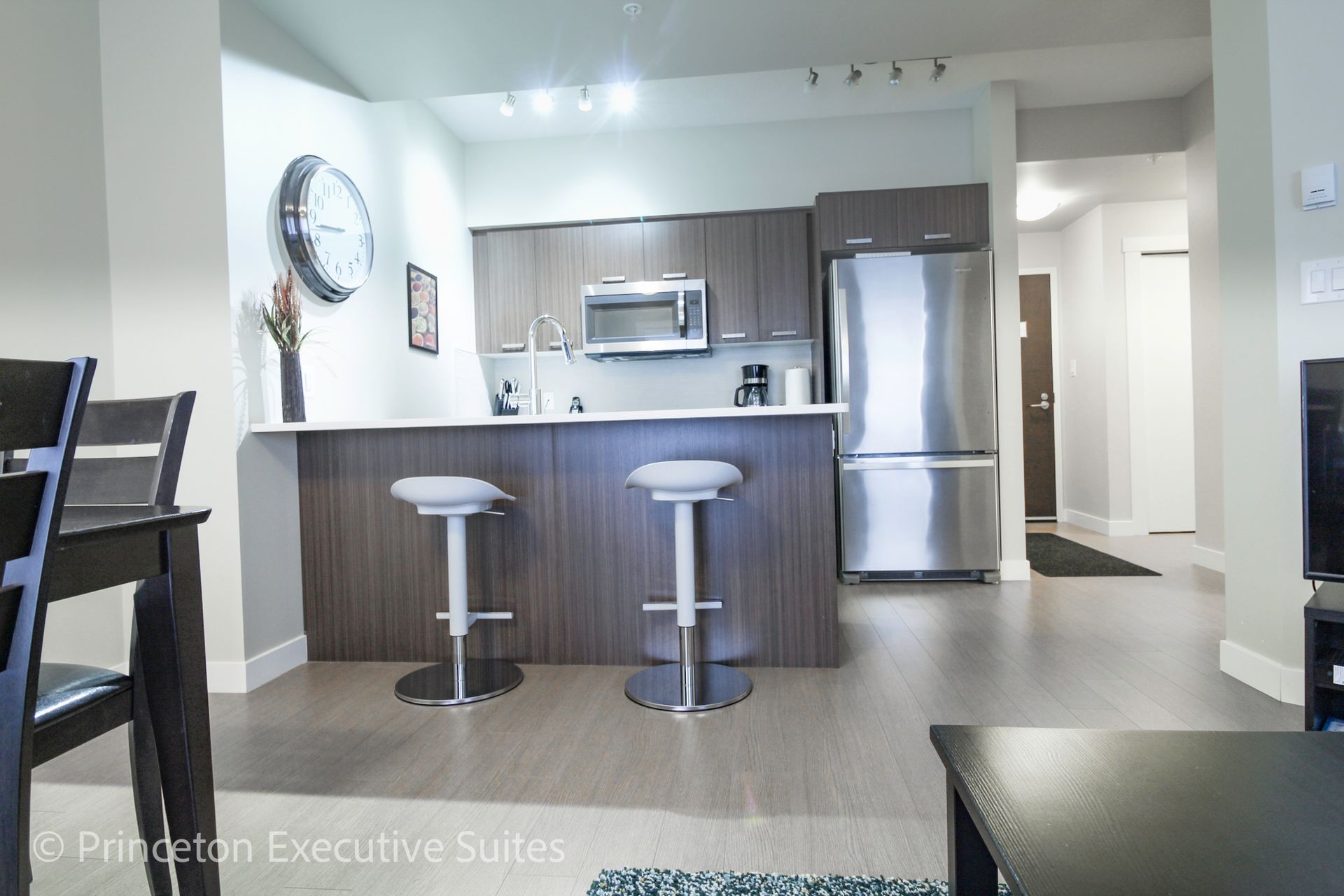 Modern kitchen with dark cabinets, stainless steel appliances, and a breakfast bar with two stools.