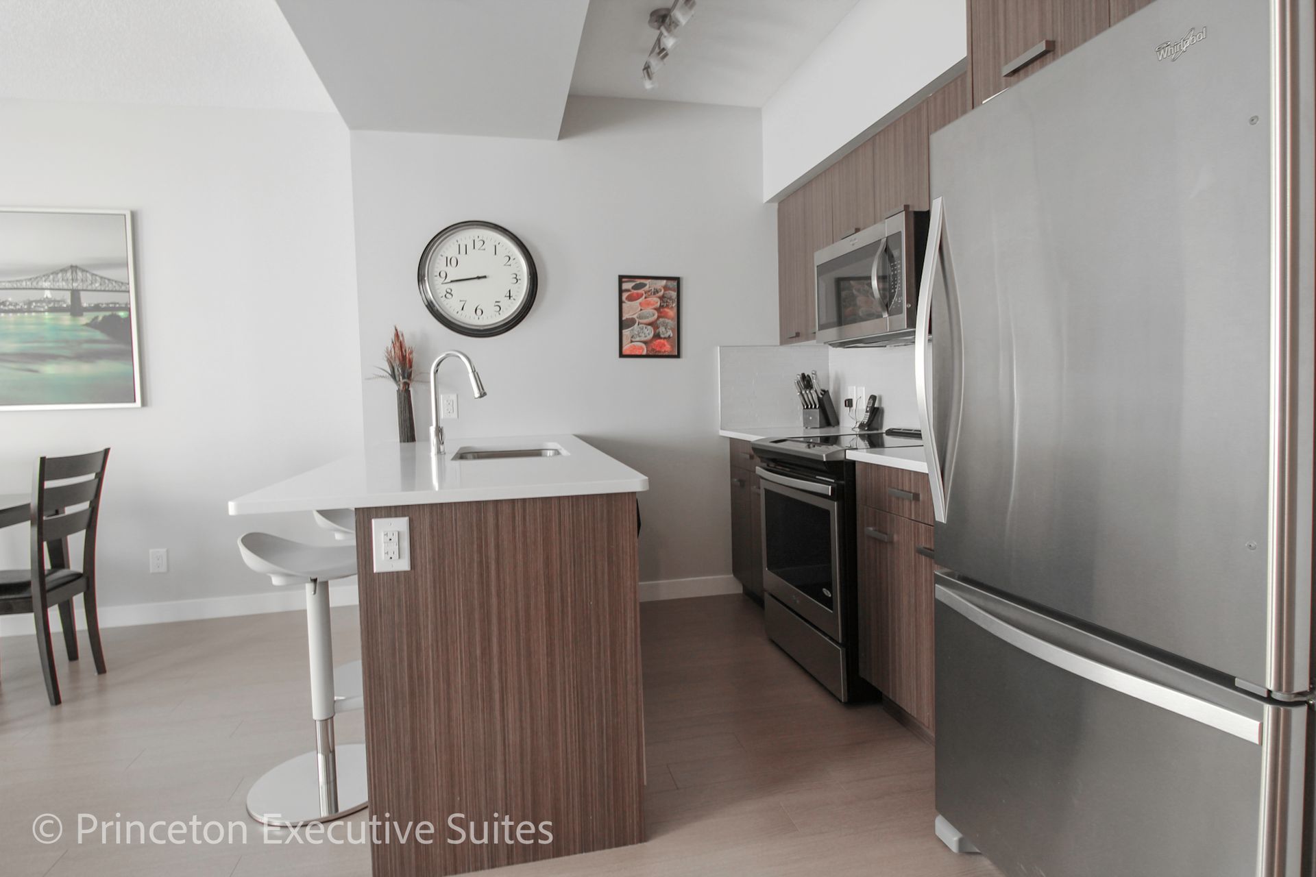 Modern kitchen with island, stainless steel appliances, and large clock.