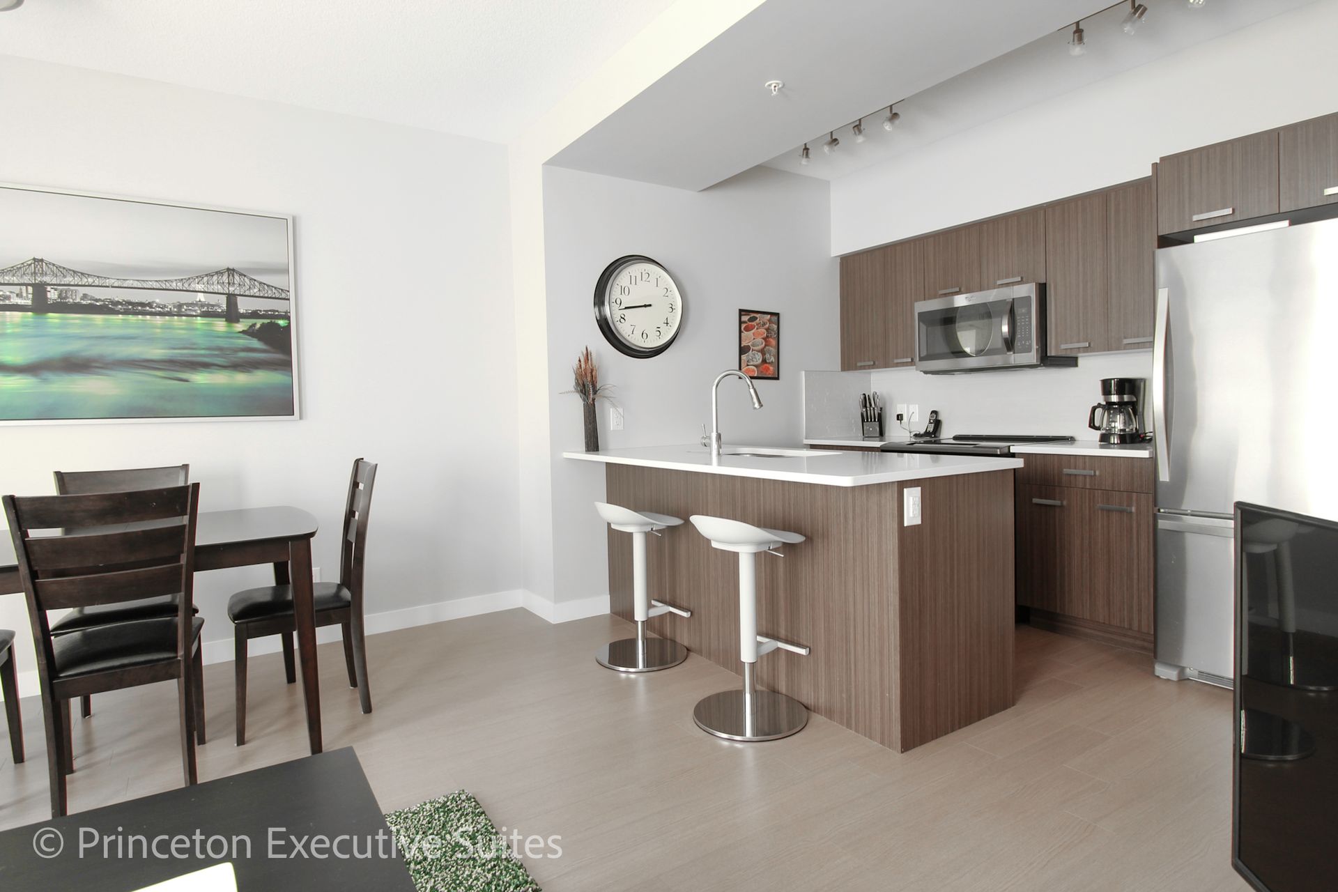 Modern kitchen with island and bar stools, dining table, stainless steel appliances, and art.