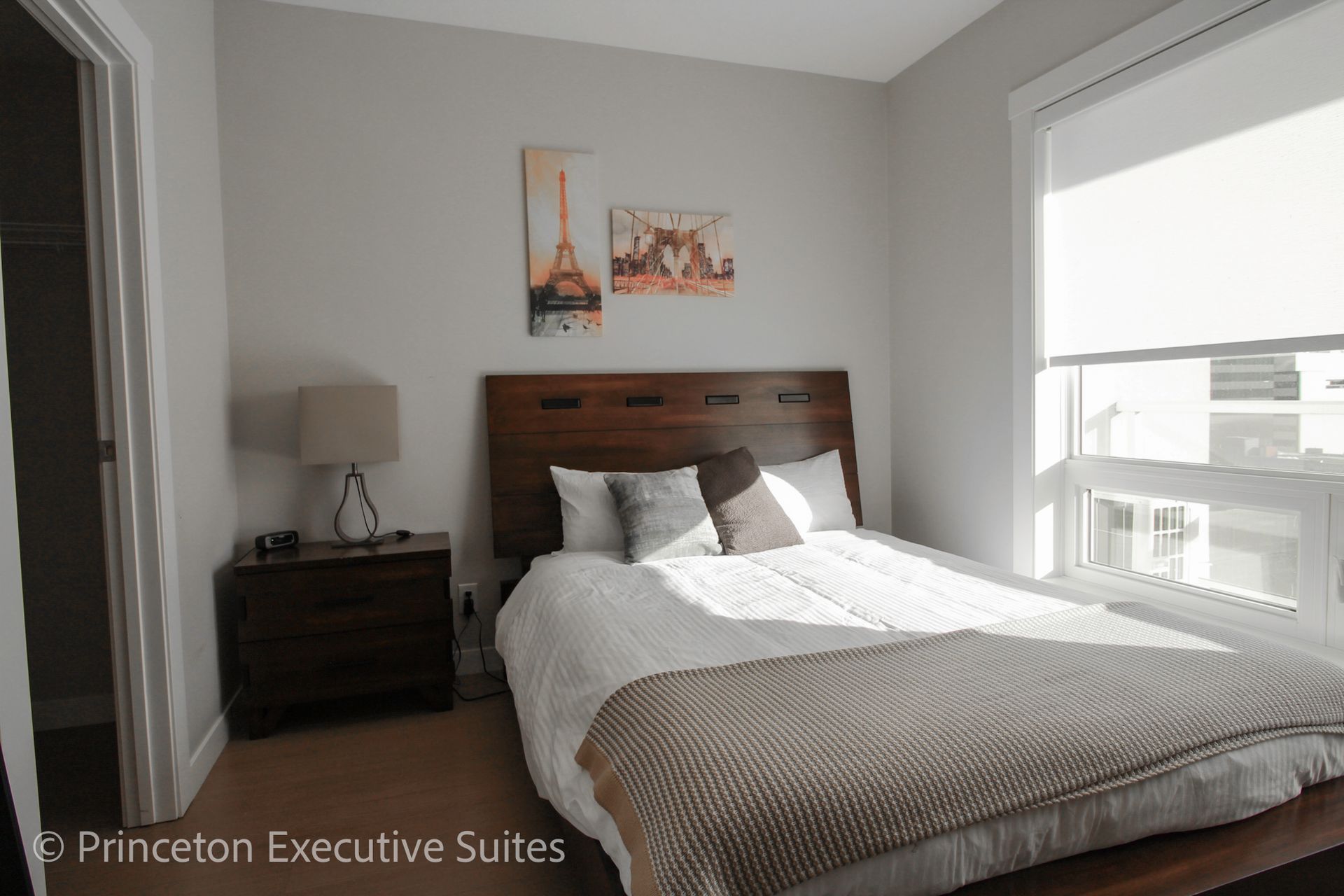 Bedroom with bed, nightstand, window with blinds, and art on the wall.