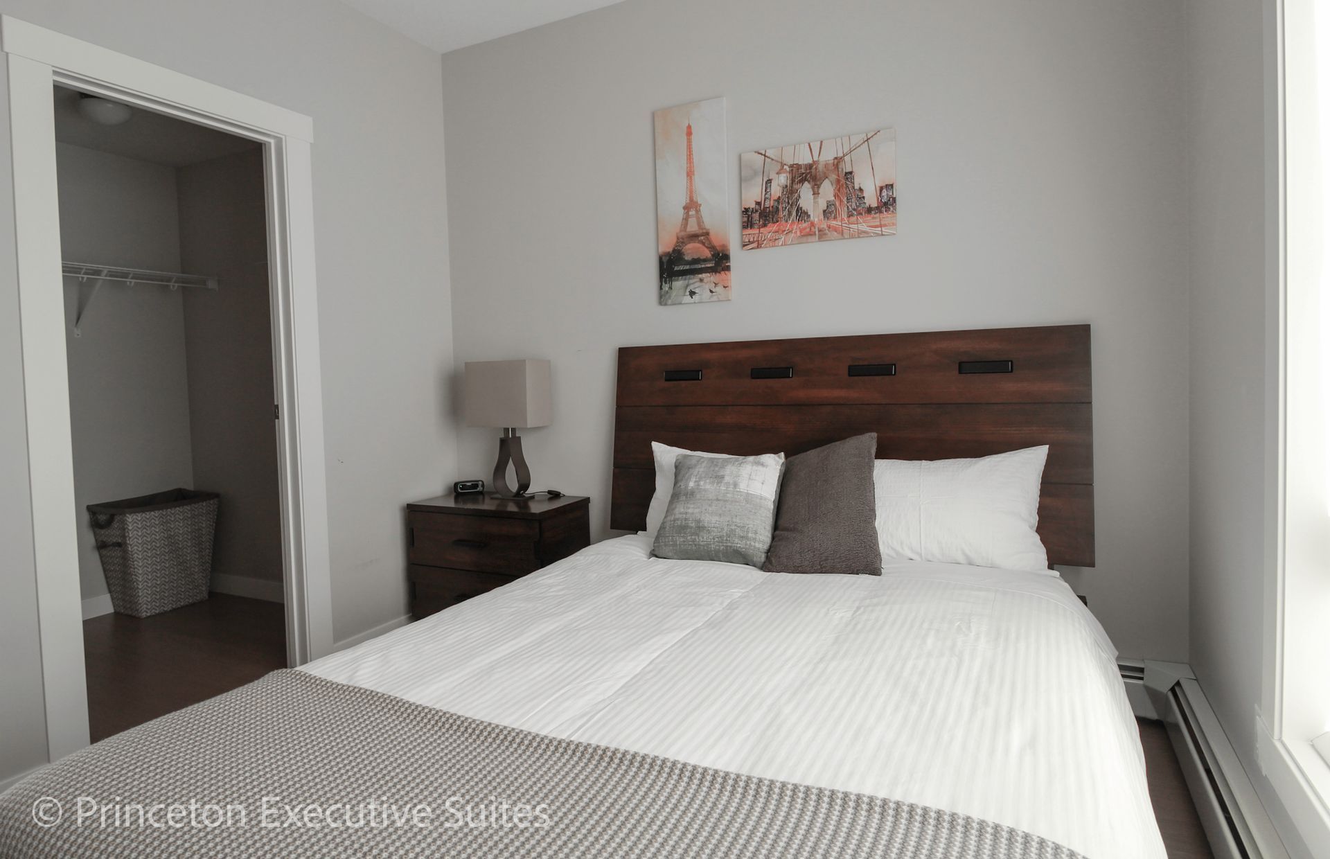 Bedroom with bed, nightstand, artwork, and closet. Gray walls, wood headboard, and striped bedding.