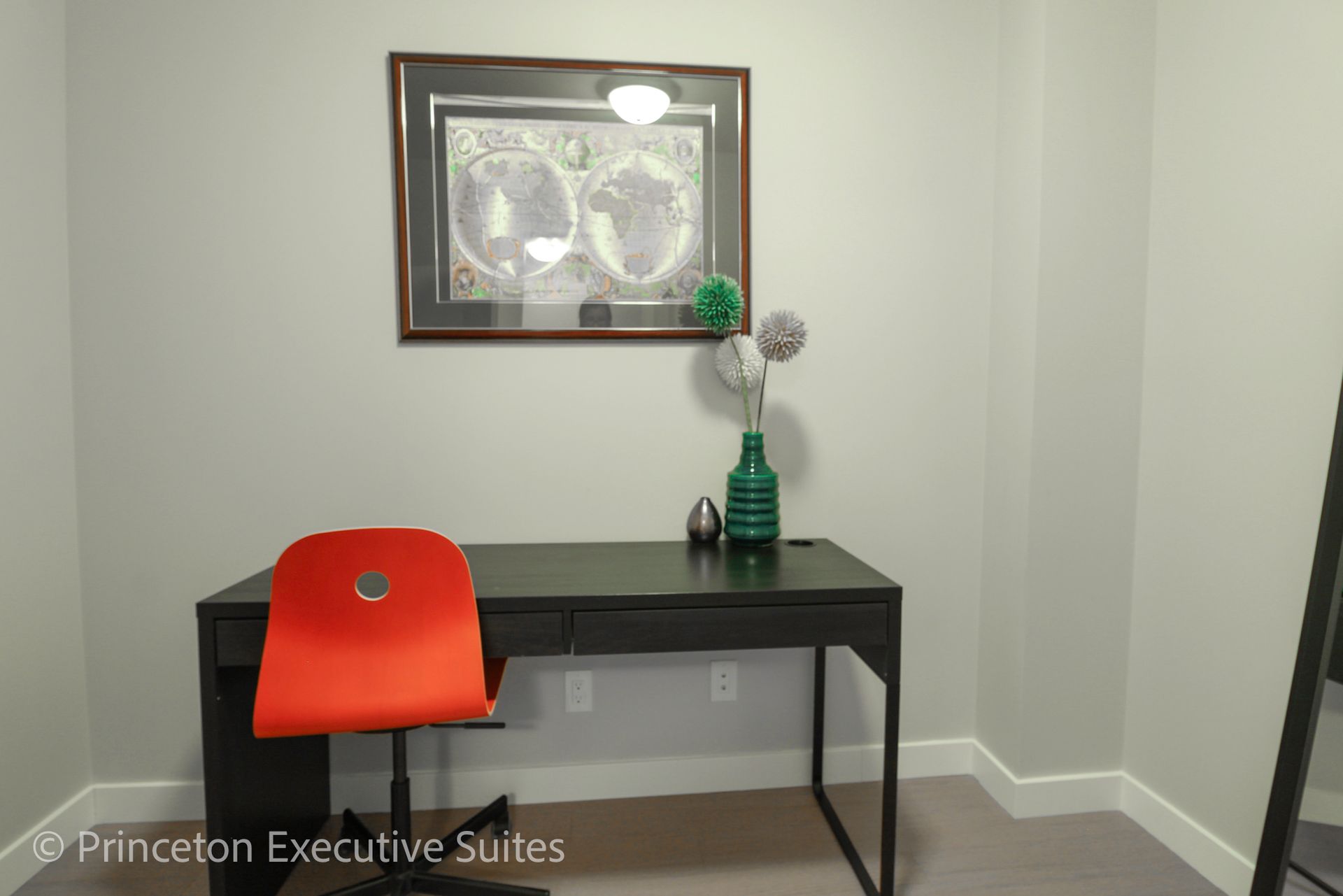 A modern office with a black desk, orange chair, decor, and a framed map on a gray wall.