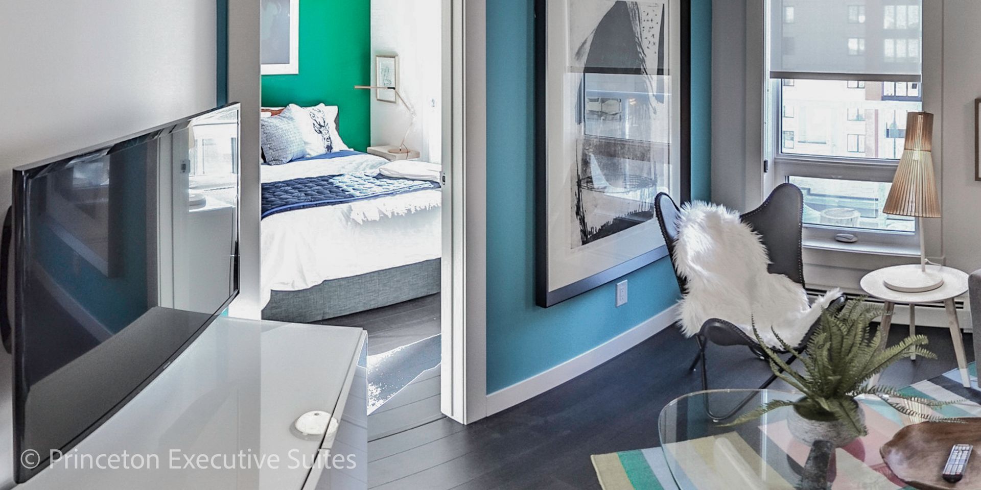 Modern apartment interior with teal walls, butterfly chair, and a view to a bedroom.