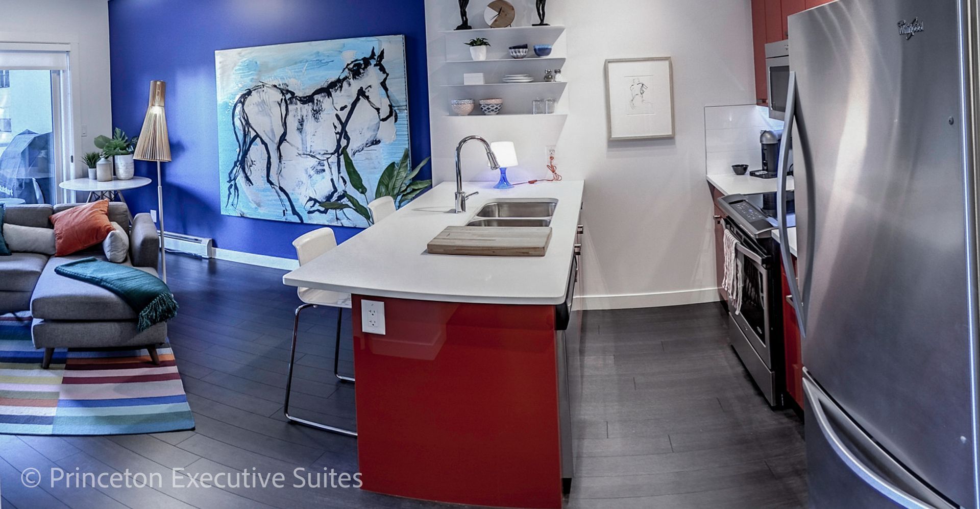 Modern kitchen with red island, stainless steel appliances, and blue accent wall with horse art.