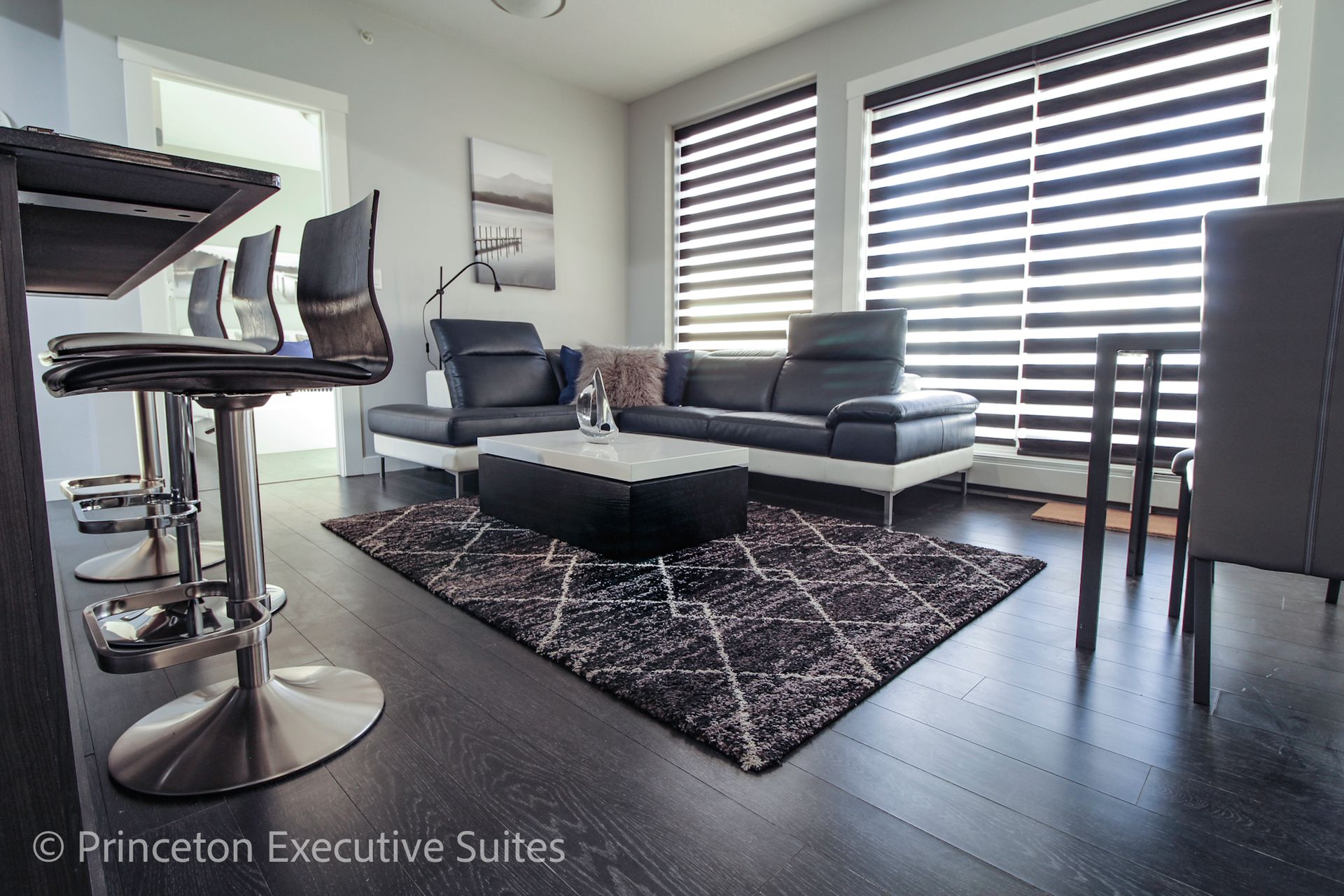 Modern living room with black leather sofa, bar stools, and a patterned rug.