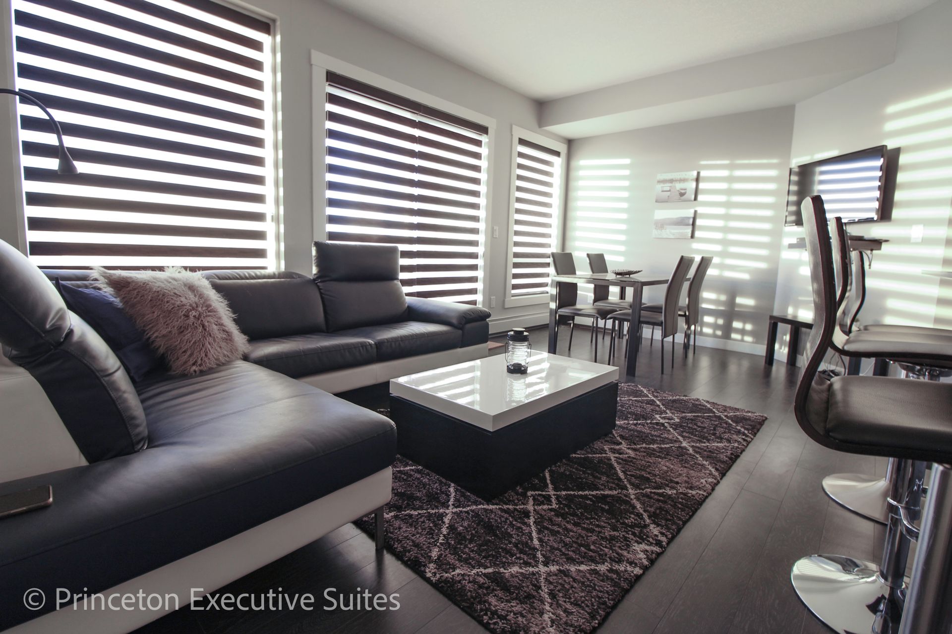 Modern living room with dark leather sectional, dining area, and zebra blinds.