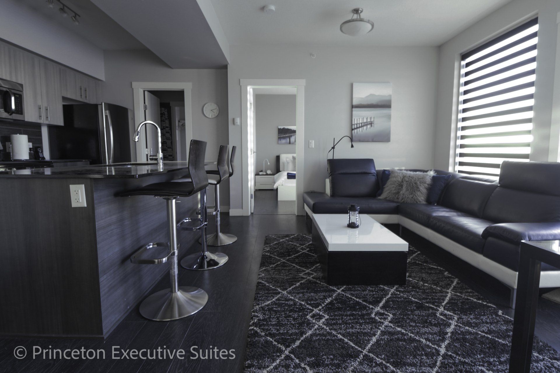 Open concept kitchen with cabinets black granite counter tops, stainless steel appliances navy blue couch black barstools
