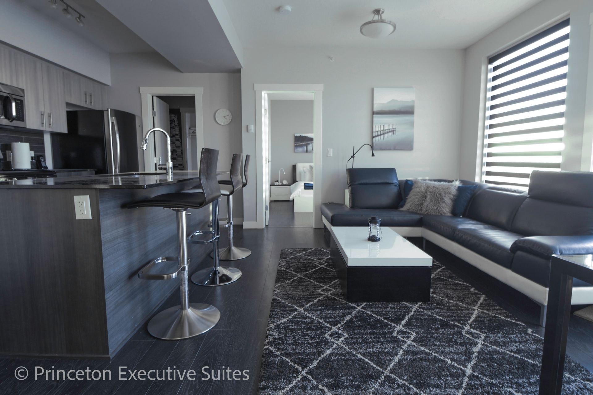 Modern apartment interior with kitchen, living room, and seating. Gray and blue tones, bright natural light.