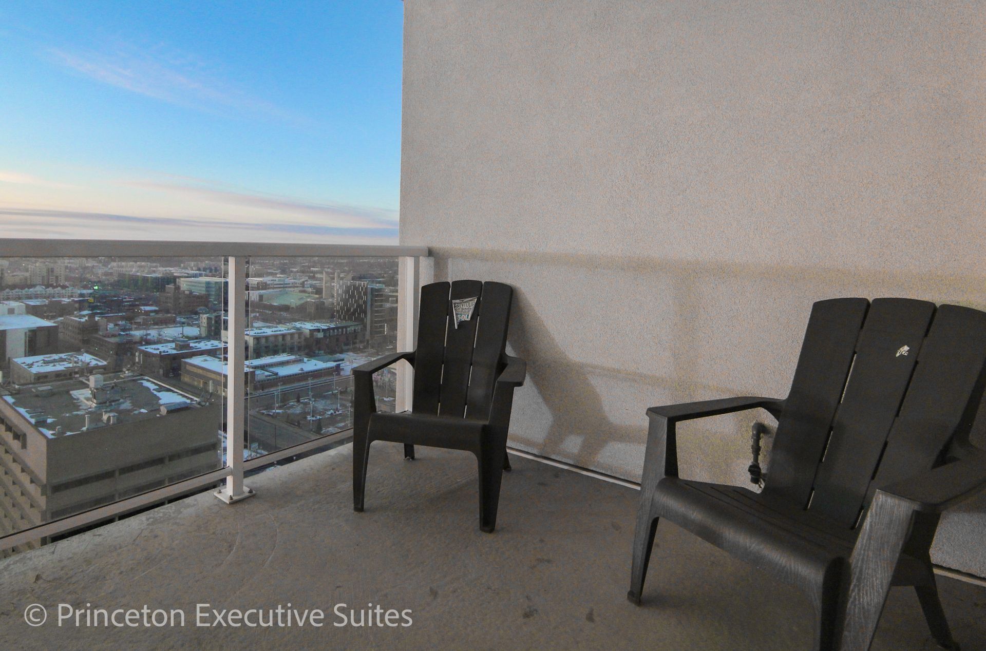 Two black chairs on a balcony overlooking a city skyline with a blue sky.