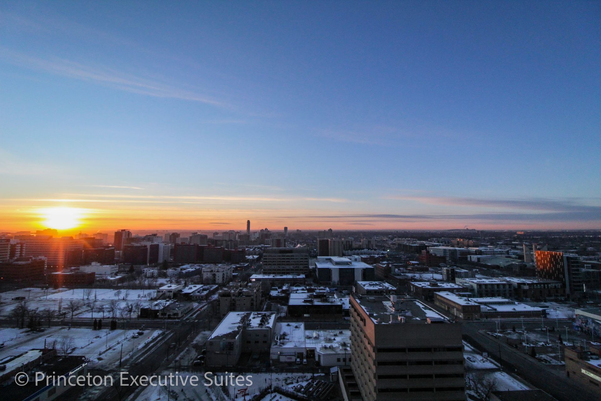 Sunset over city buildings with some snow cover.
