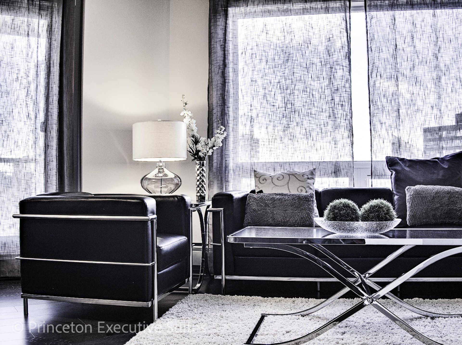 Black couch, black chair and coffee table in front of a curtained window Edmonton furnished executive apartments