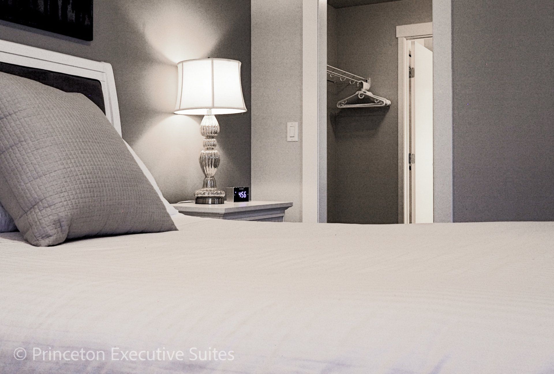 Bedroom whit white linens grey pillow and lamp on in a bedside table in the background  edmonton executive condos