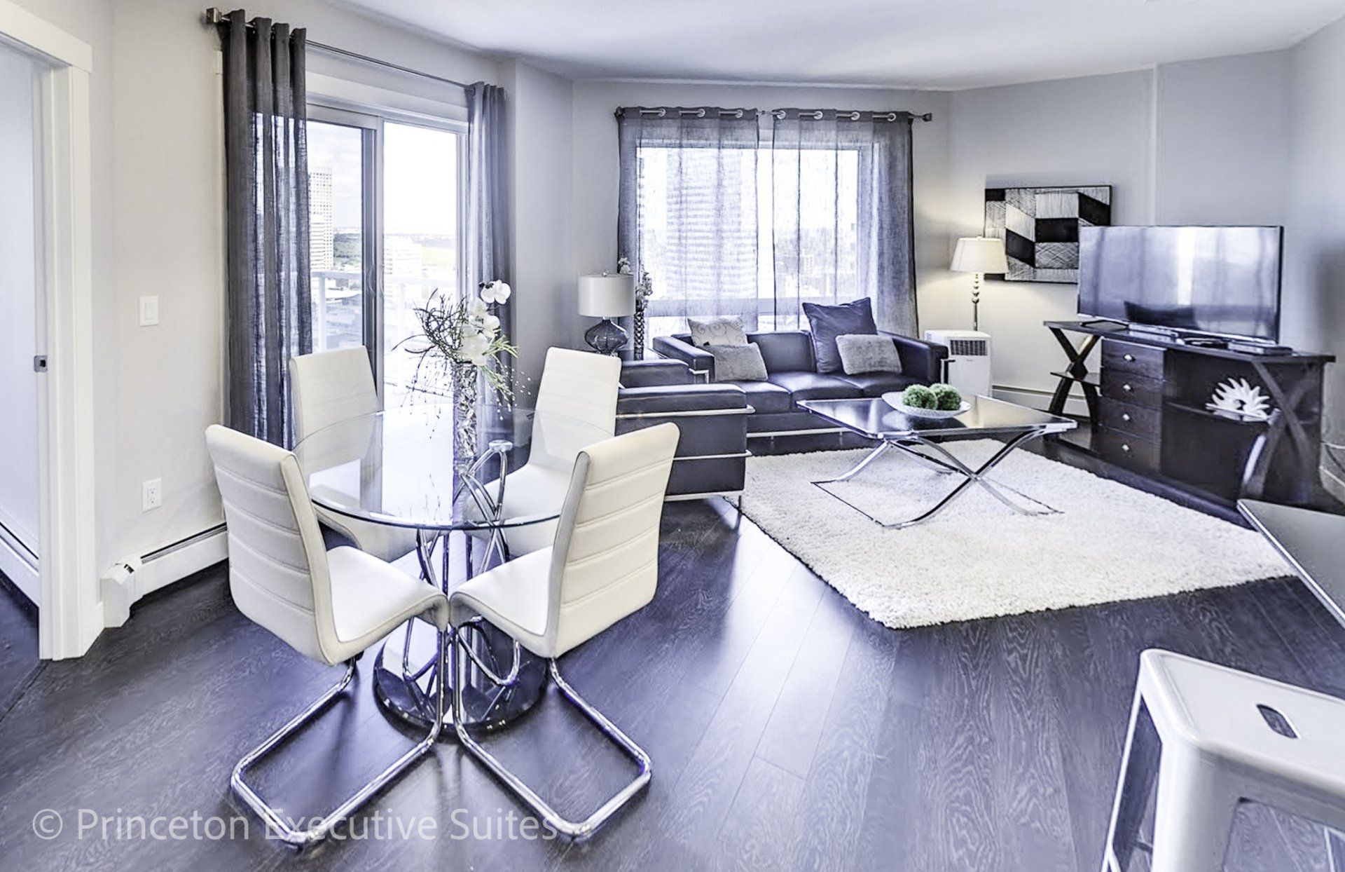Modern Dining and living area with white chairs and glass table living area with black couch and chair in the back ground