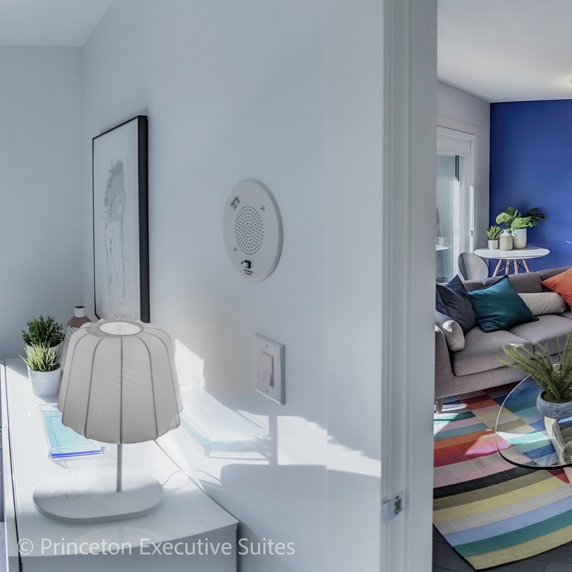 Hallway with a desk and lamp, leading into a living room with colorful rug and blue wall.