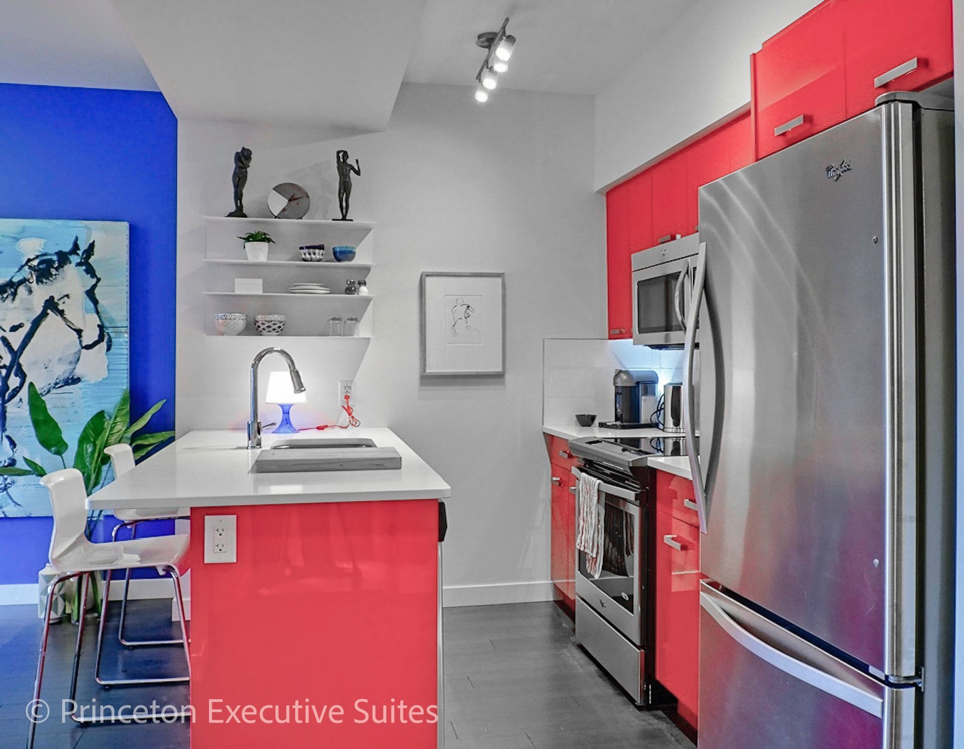 Bright red and white kitchen with stainless steel appliances, blue accent wall, and artwork.