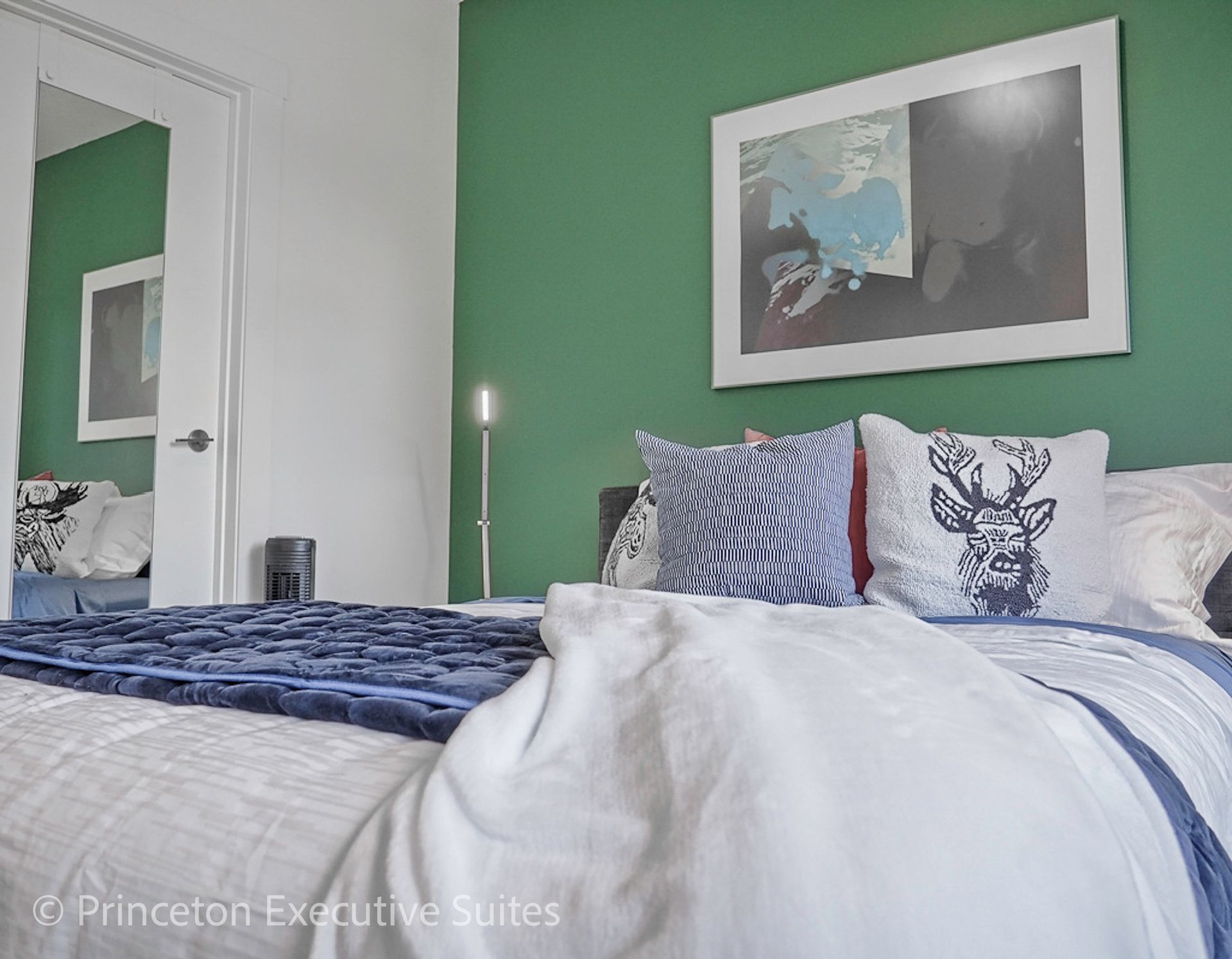 Bedroom with green accent wall, bed with pillows and artwork.