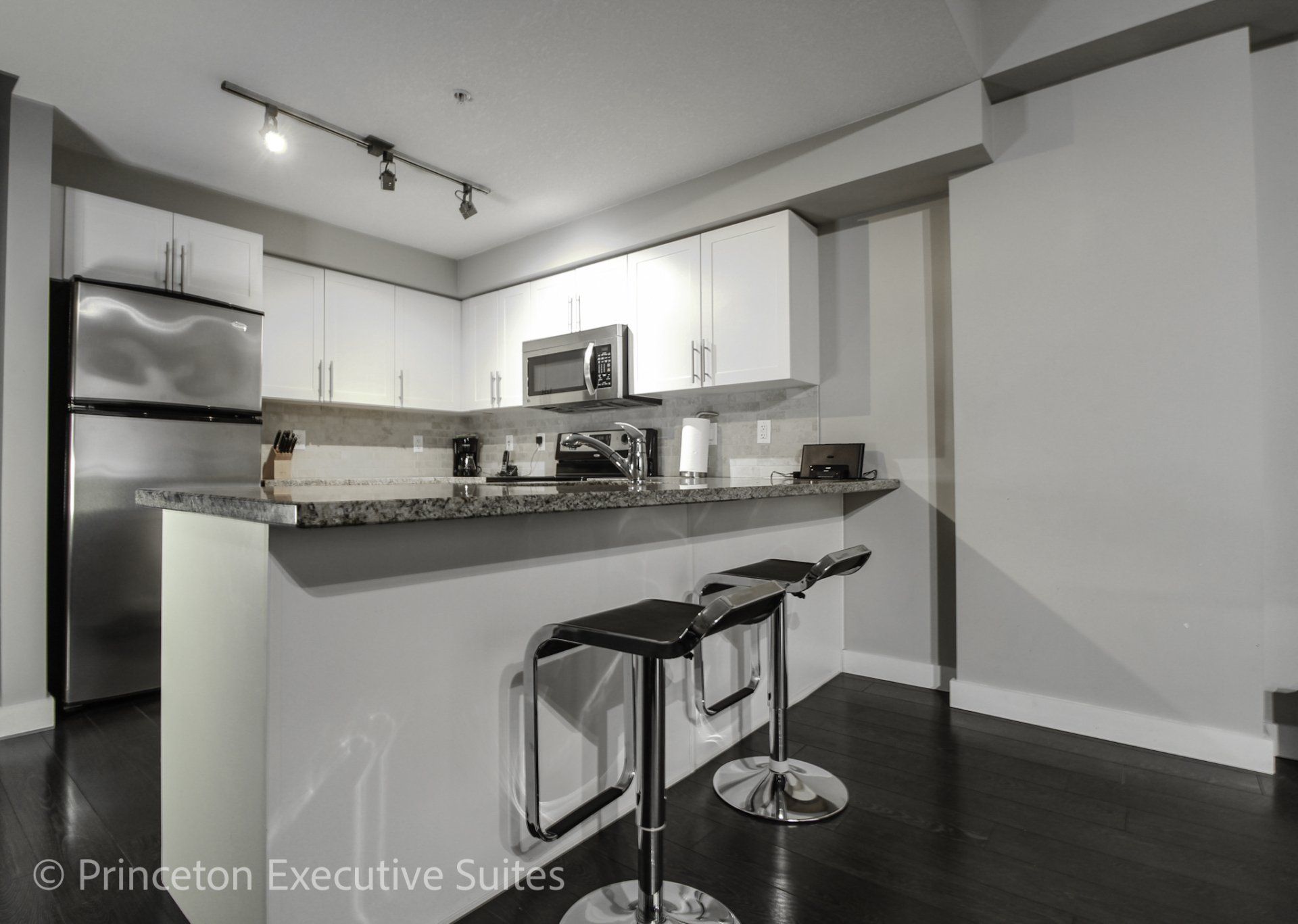 white kitchen with  granite counter tops metal barstools in front of eating bar in an Edmonton furnished suite