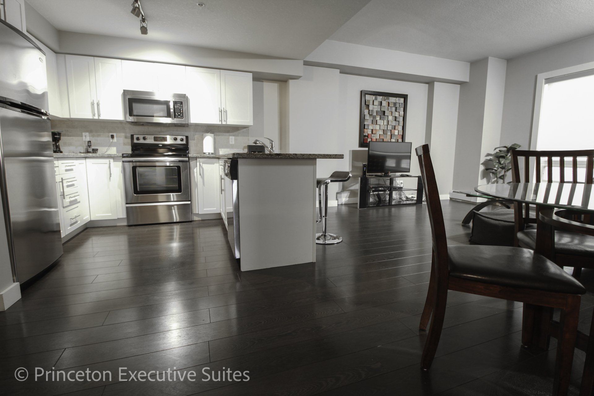 Dark hardwood flooring white  kitchen cupboards and stainless steel appliances are a feature of this Edmonton furnished suite