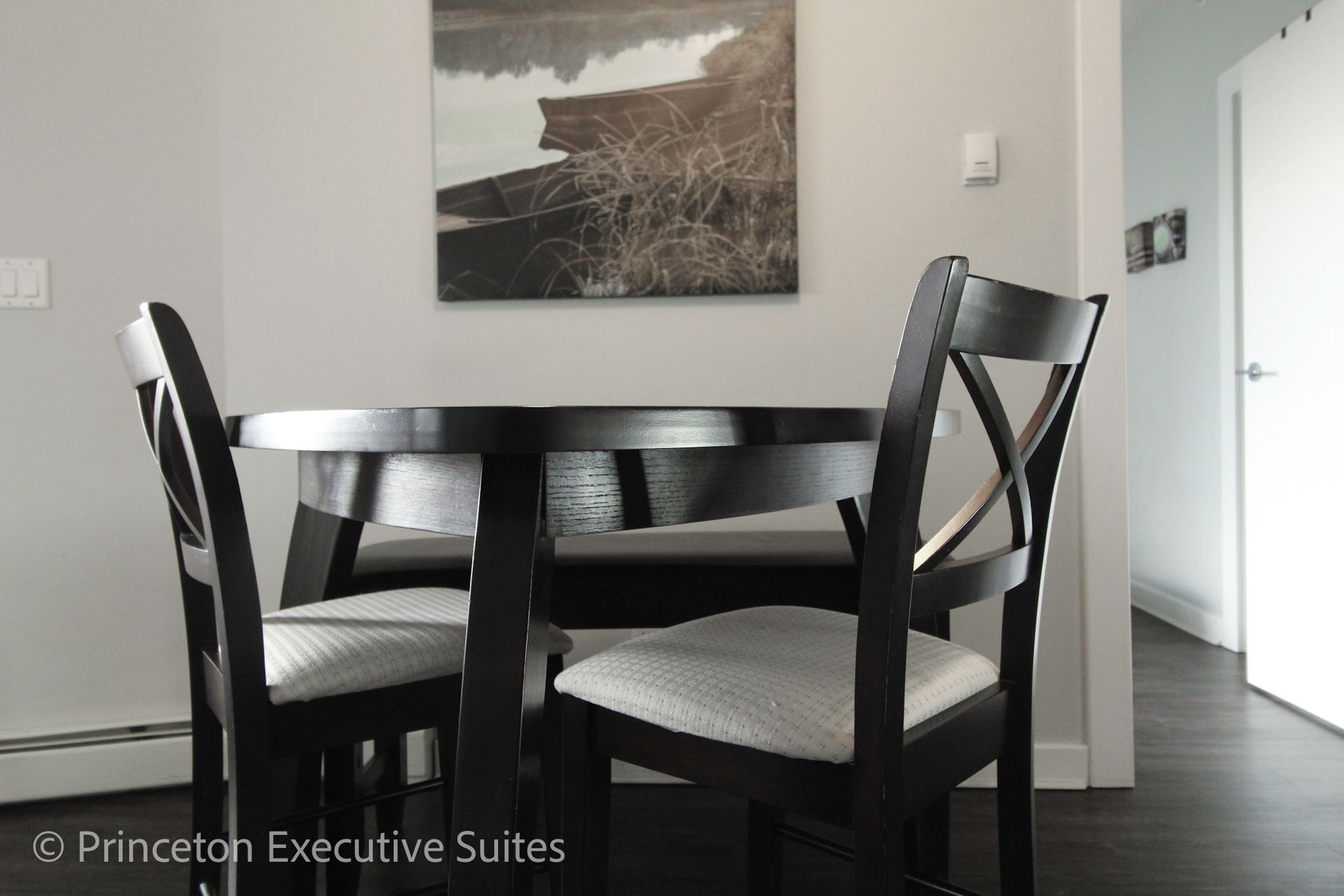 Round black table with three matching chairs in a dining area, painting on the wall.