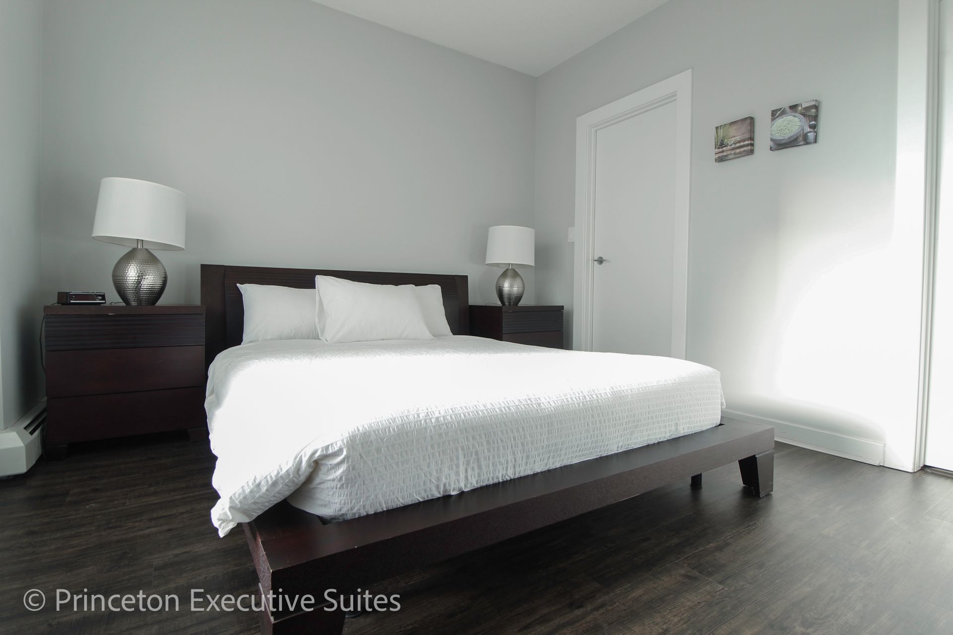 Bedroom with dark wooden bed and furniture, gray walls, white bedding and lamps.