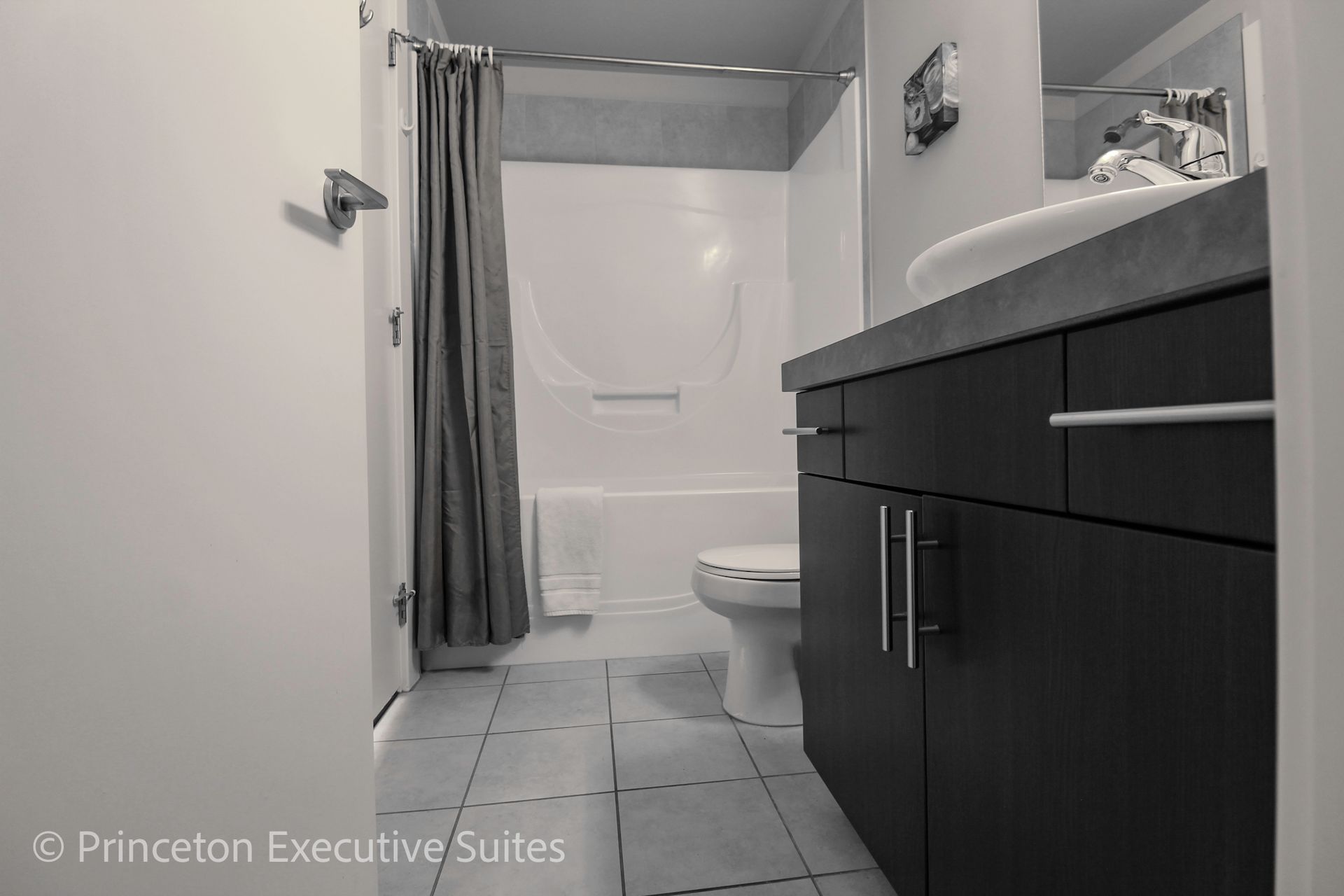 Bathroom with dark cabinets, white sink, and tub with a gray curtain.