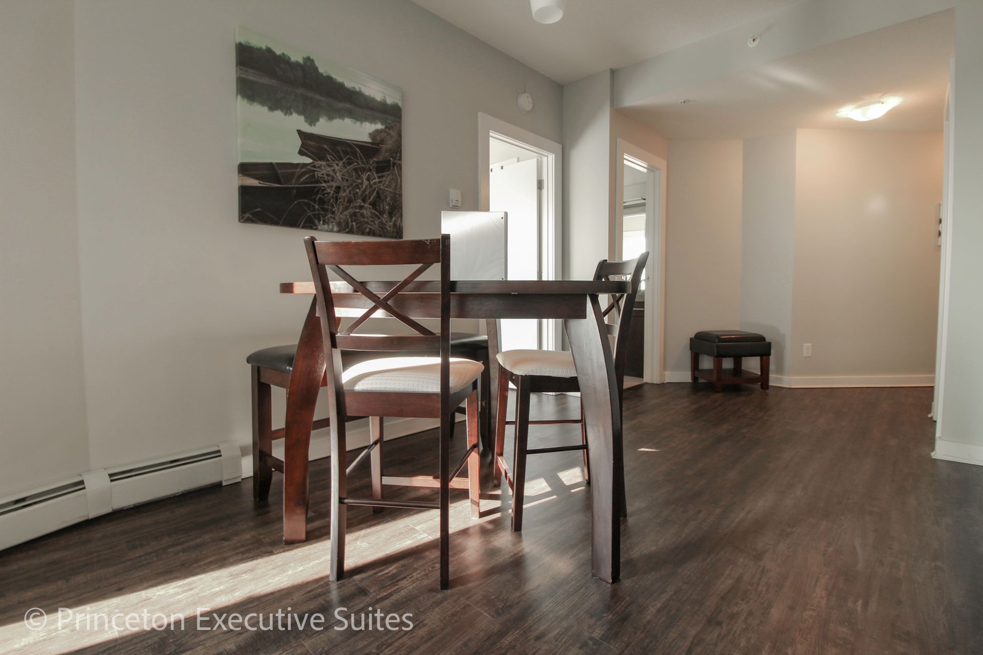 Dining area with dark wood table and chairs, art on wall, dark wood floor, and light gray walls.