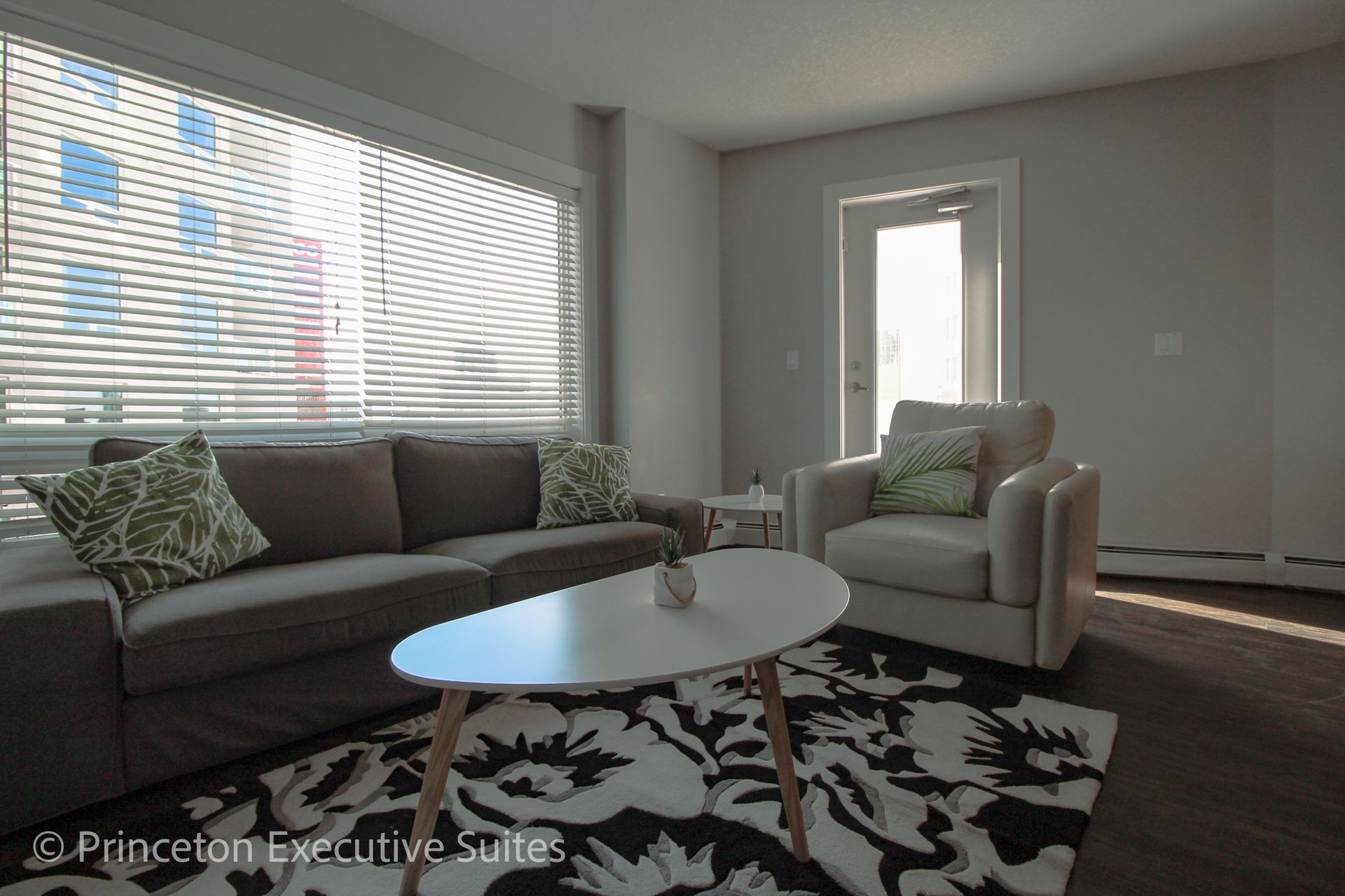 Living room with sofa, chair, and coffee table; large window with blinds.