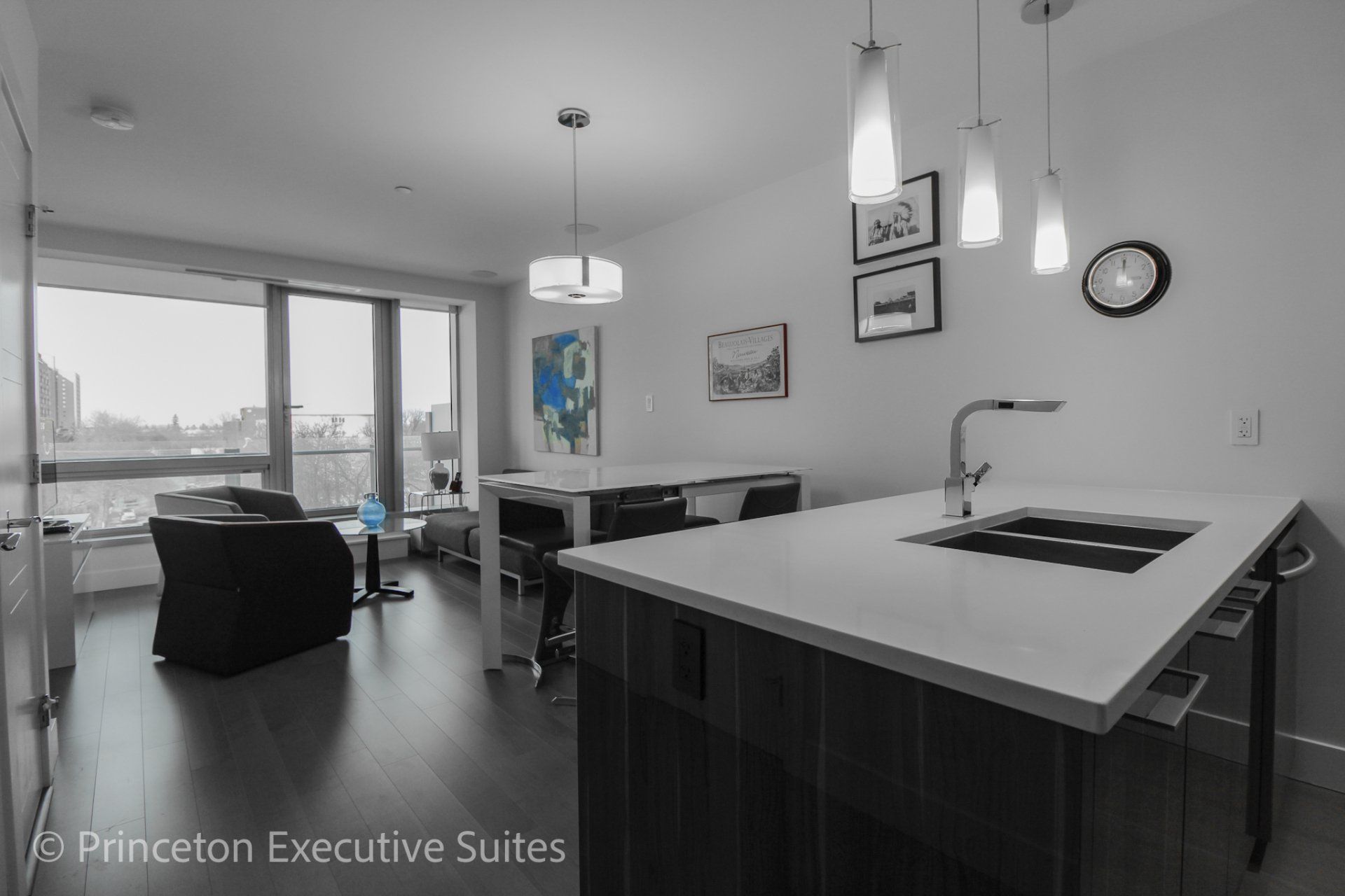 White counter top  Modern fixtures and white dining table. Grey chair  and couch in front of a large window 