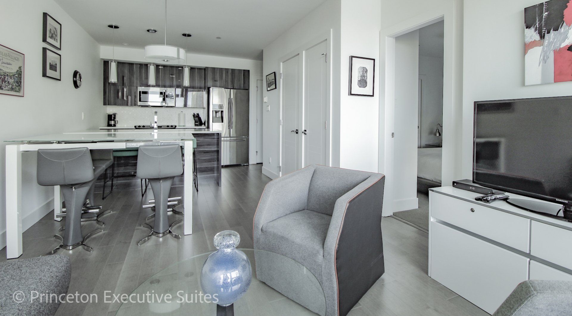 Open concept Living area with grey and black chair and lass coffee table in the foreground 