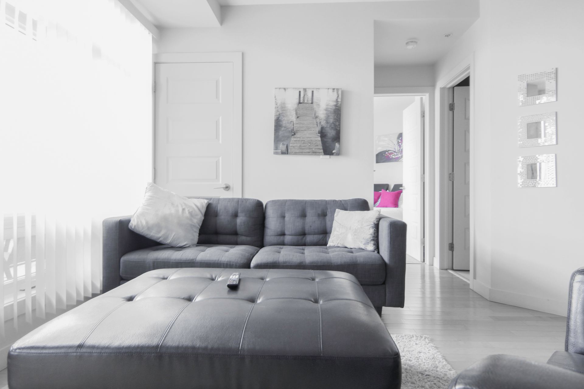 Gray and white living room with couch, ottoman, art, and doorway.