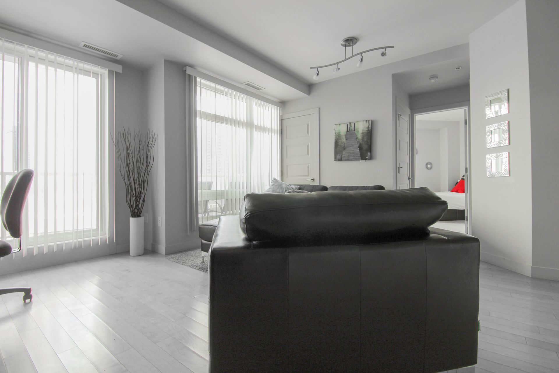 Modern living room with large windows, black leather sofa, and light wood floors.