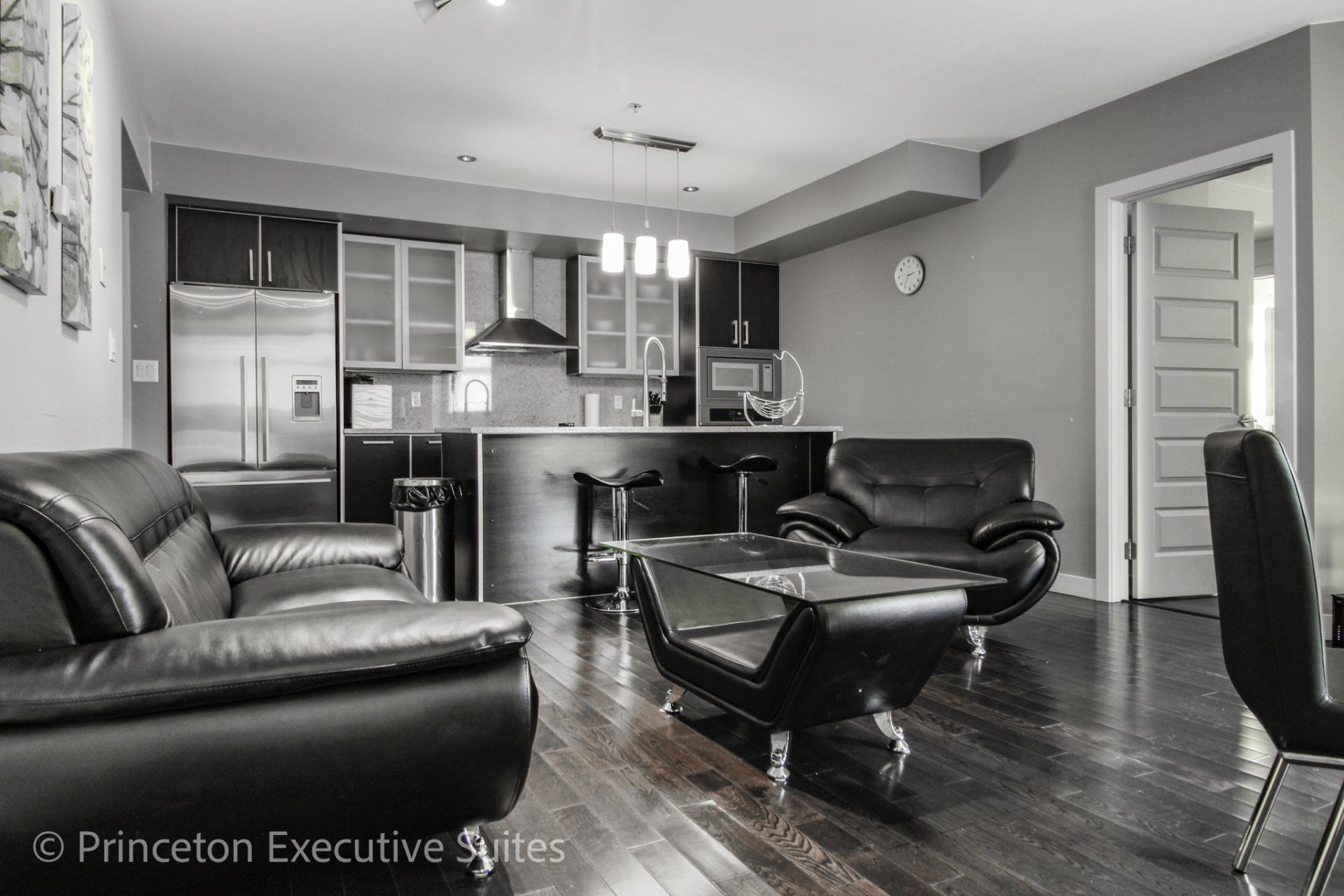 Black leather living room with espresso hardwood flooring stainless steel kitchen in back ground immaculate furnished suite 