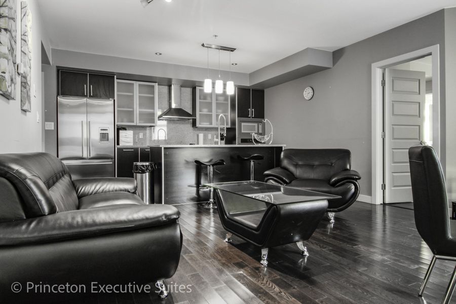 Modern living room and kitchen with black leather furniture and stainless steel appliances.