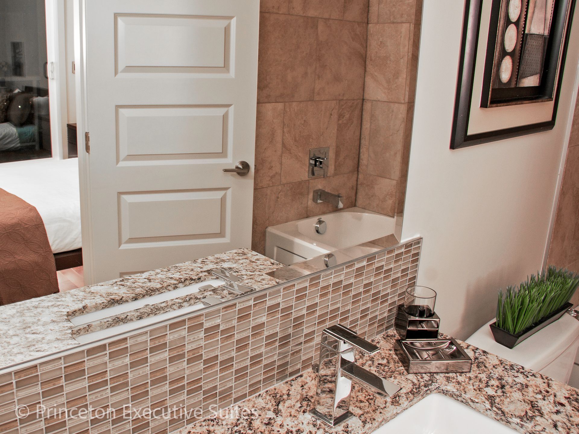 Bathroom with a mirror, sink, and tiled backsplash; a door to a bedroom is in the background.