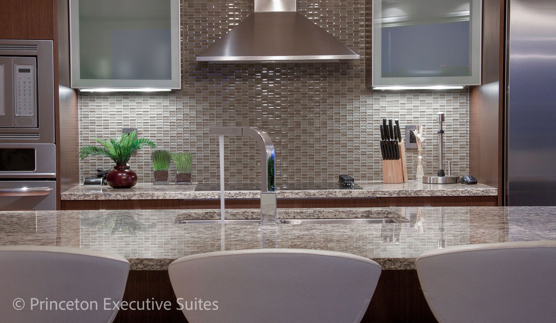Kitchen with a bar and stools, stainless steel appliances, and mosaic tile backsplash.