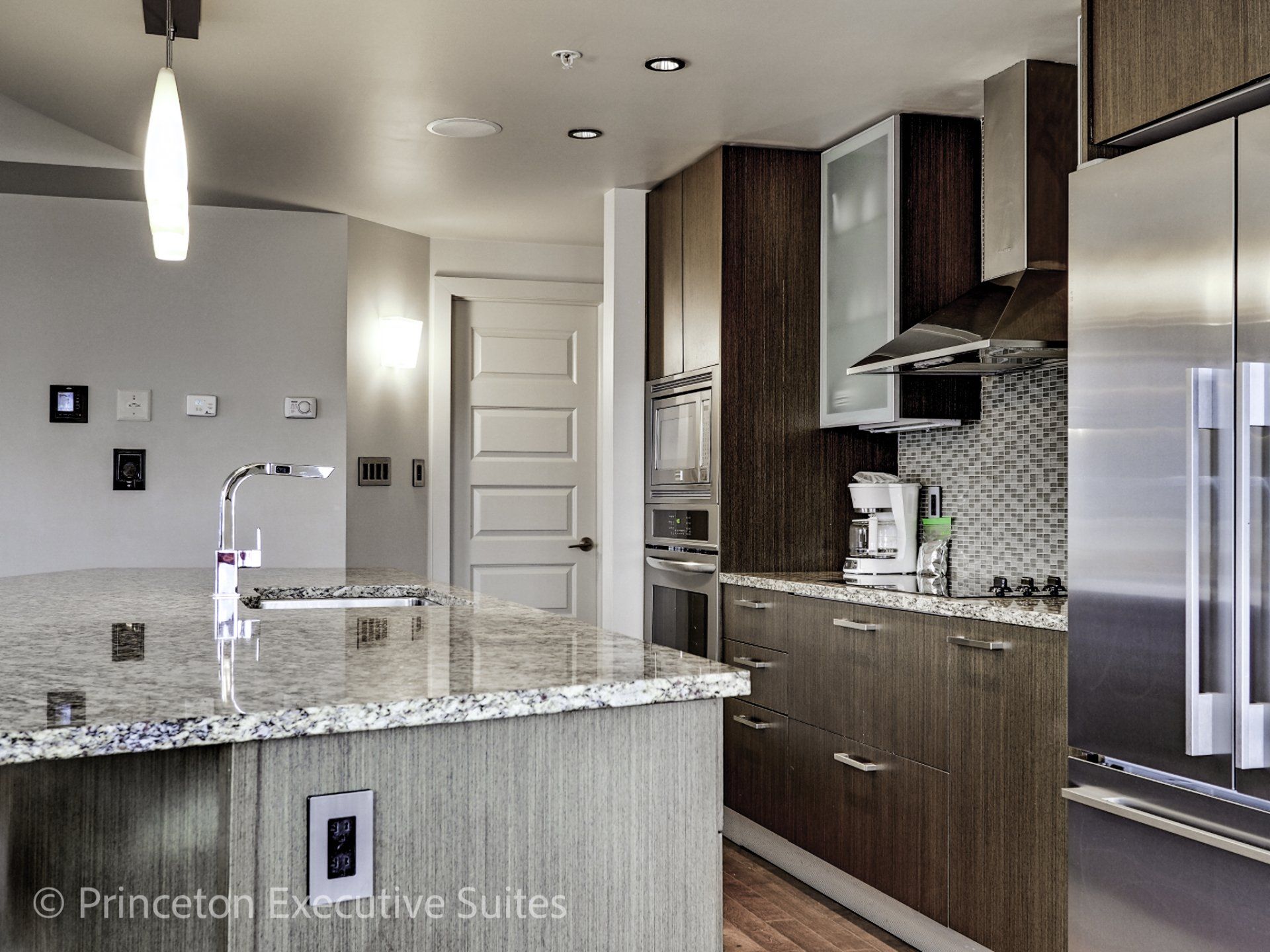 Modern kitchen with granite island, stainless steel appliances, and dark wood cabinets.