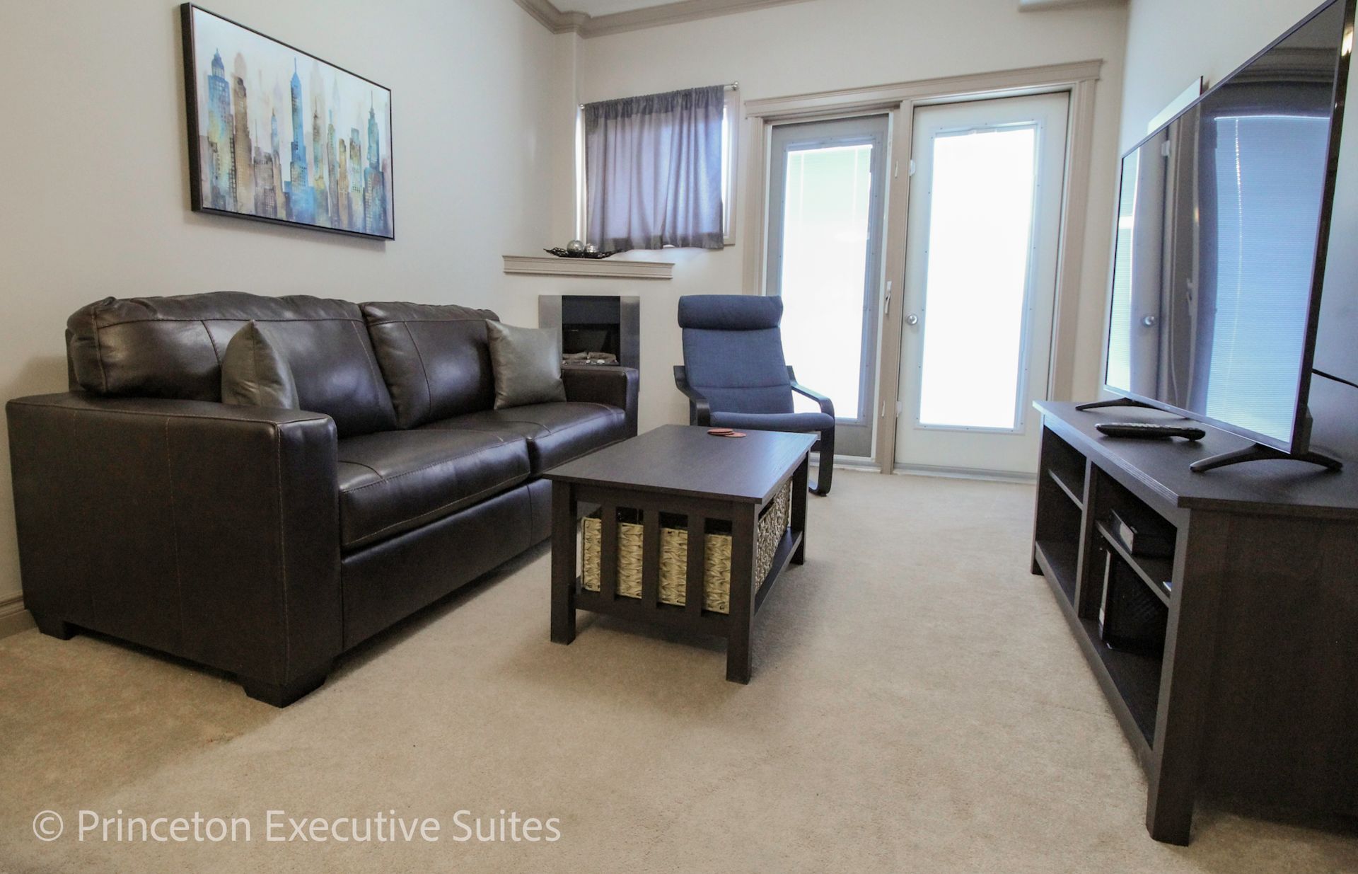Living room with brown leather couch, coffee table, TV, and glass doors.