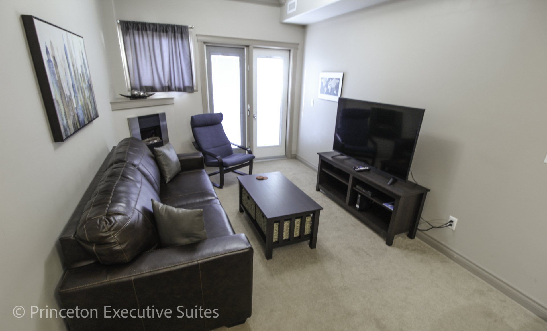 Living room of Edmonton furnished condo  TV, chair and couch  the are all brown with beige carpeting