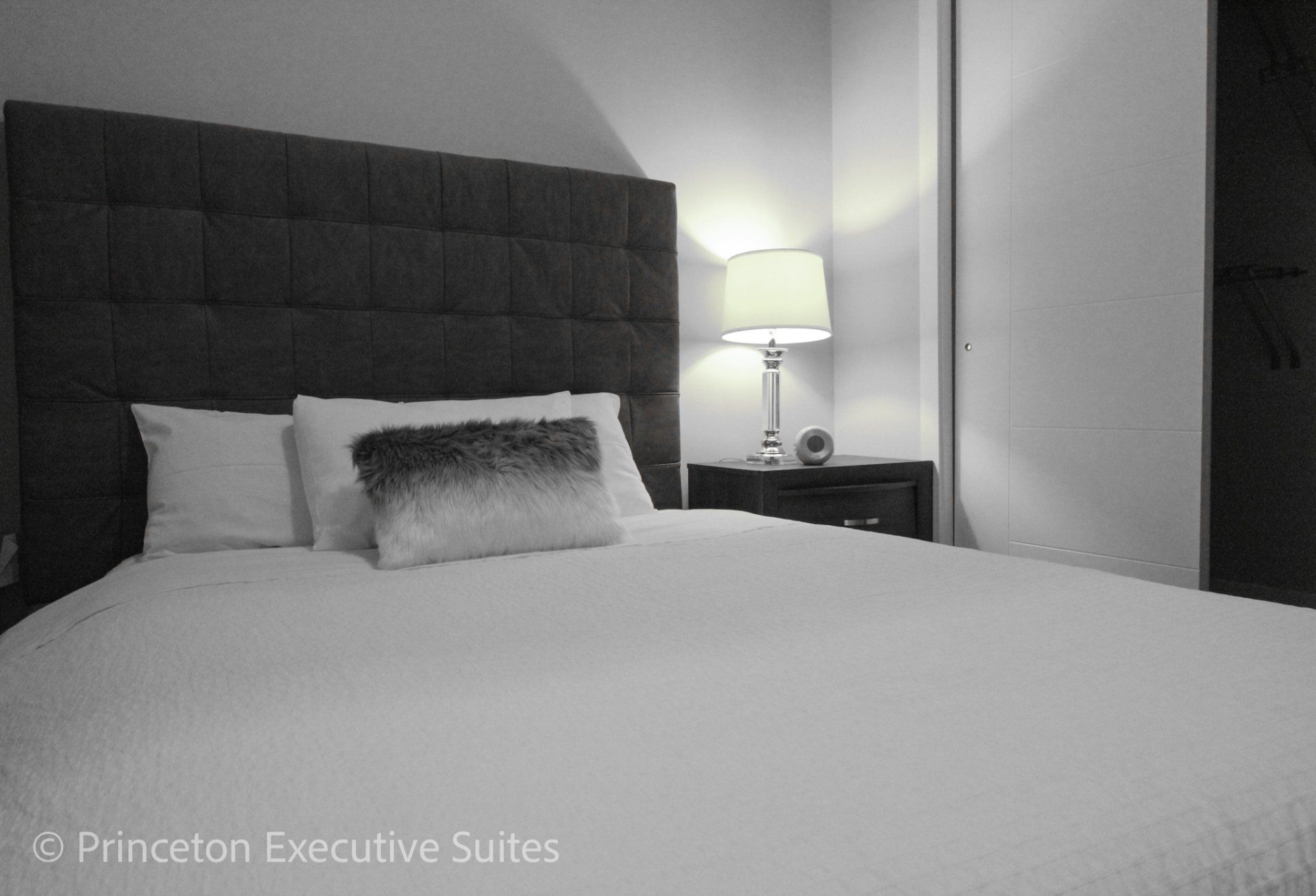 Queen sized bed with white linens nigh stand and glass lamp