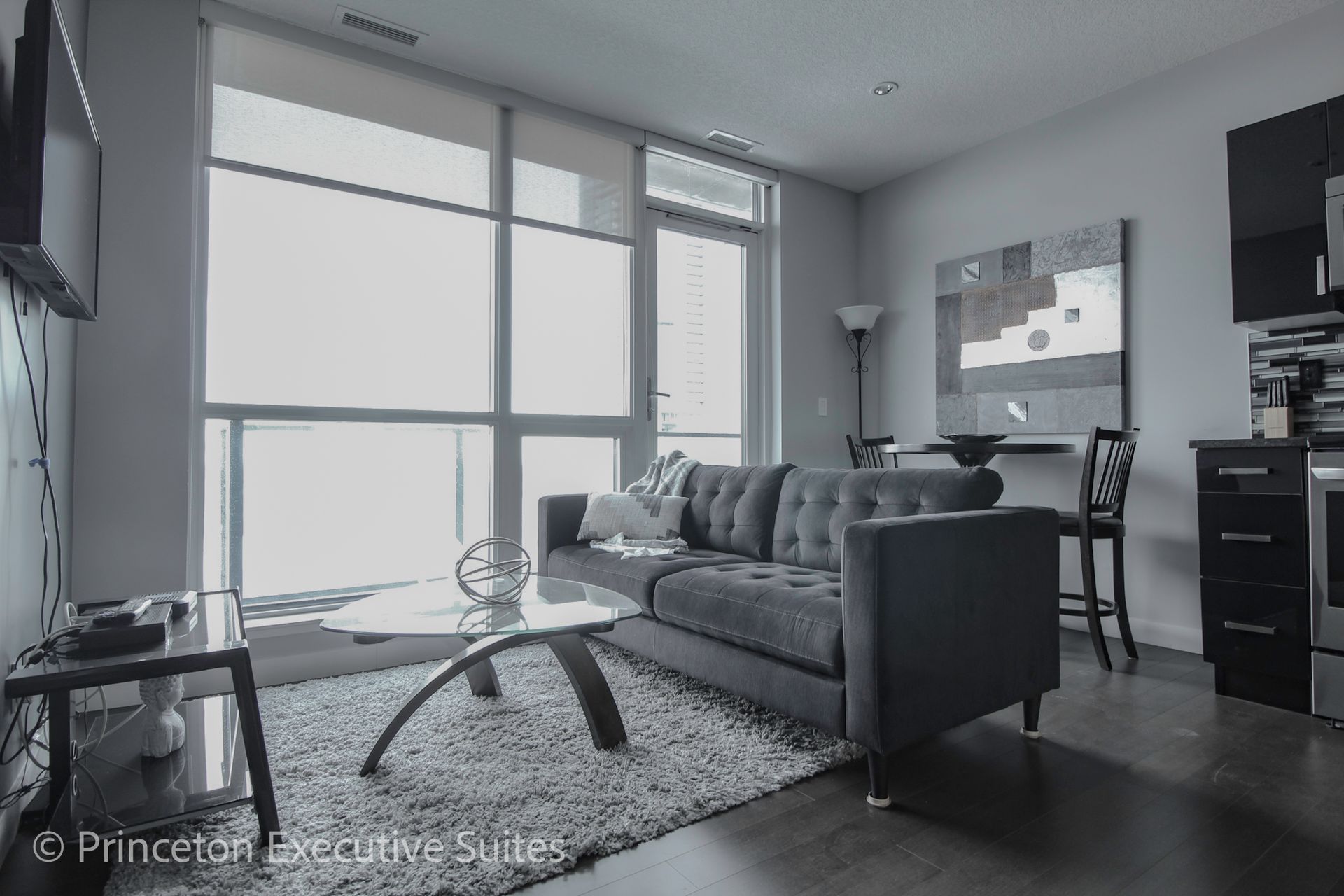 Modern living room with sofa, coffee table, large windows, and artwork.