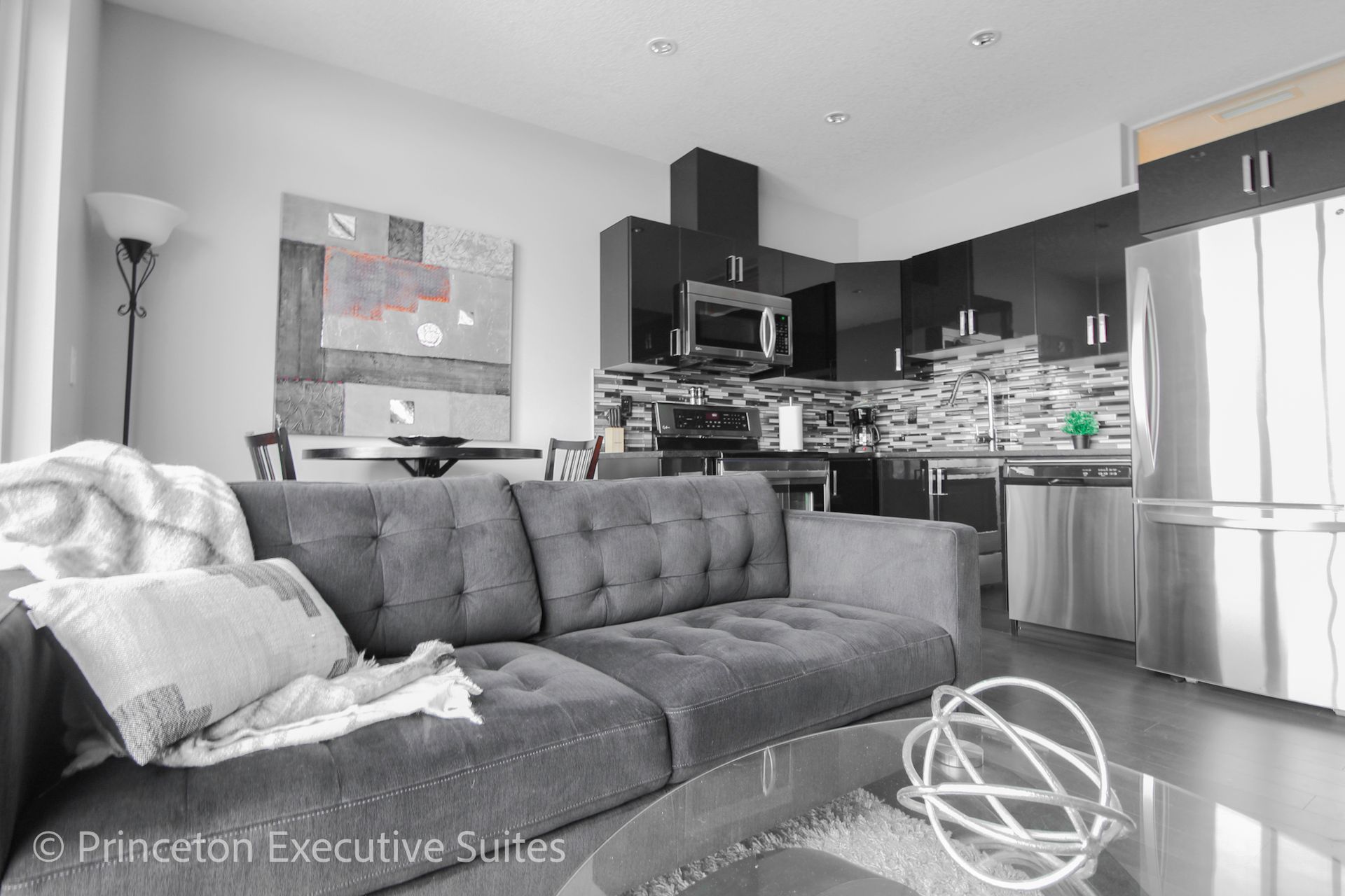 Modern living room with gray sofa, open kitchen, and stainless steel appliances.