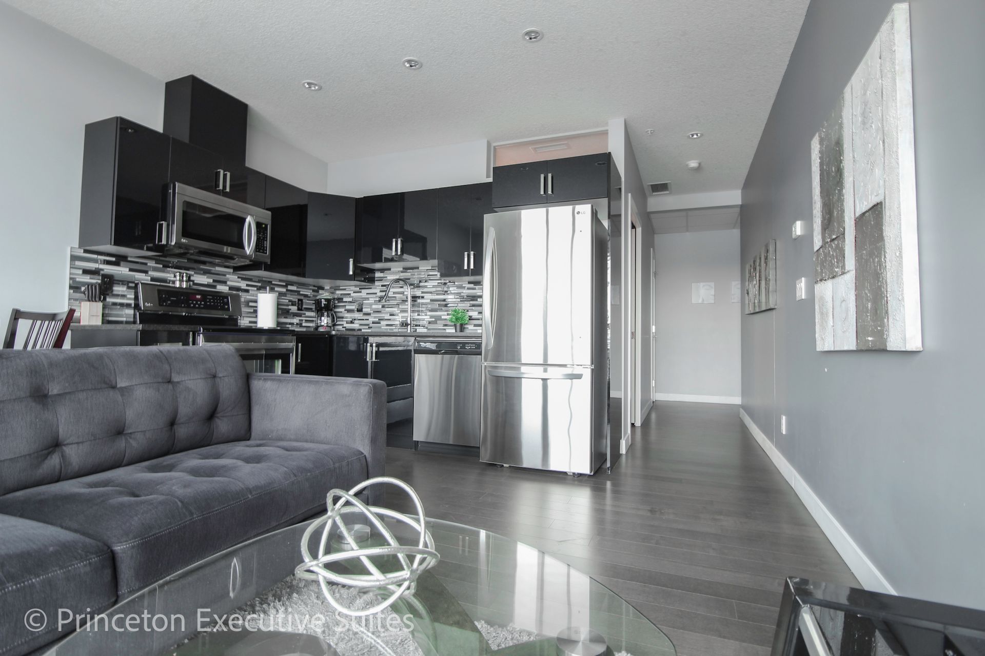 Modern open-concept condo: gray sofa, black kitchen, stainless steel fridge, and gray walls.