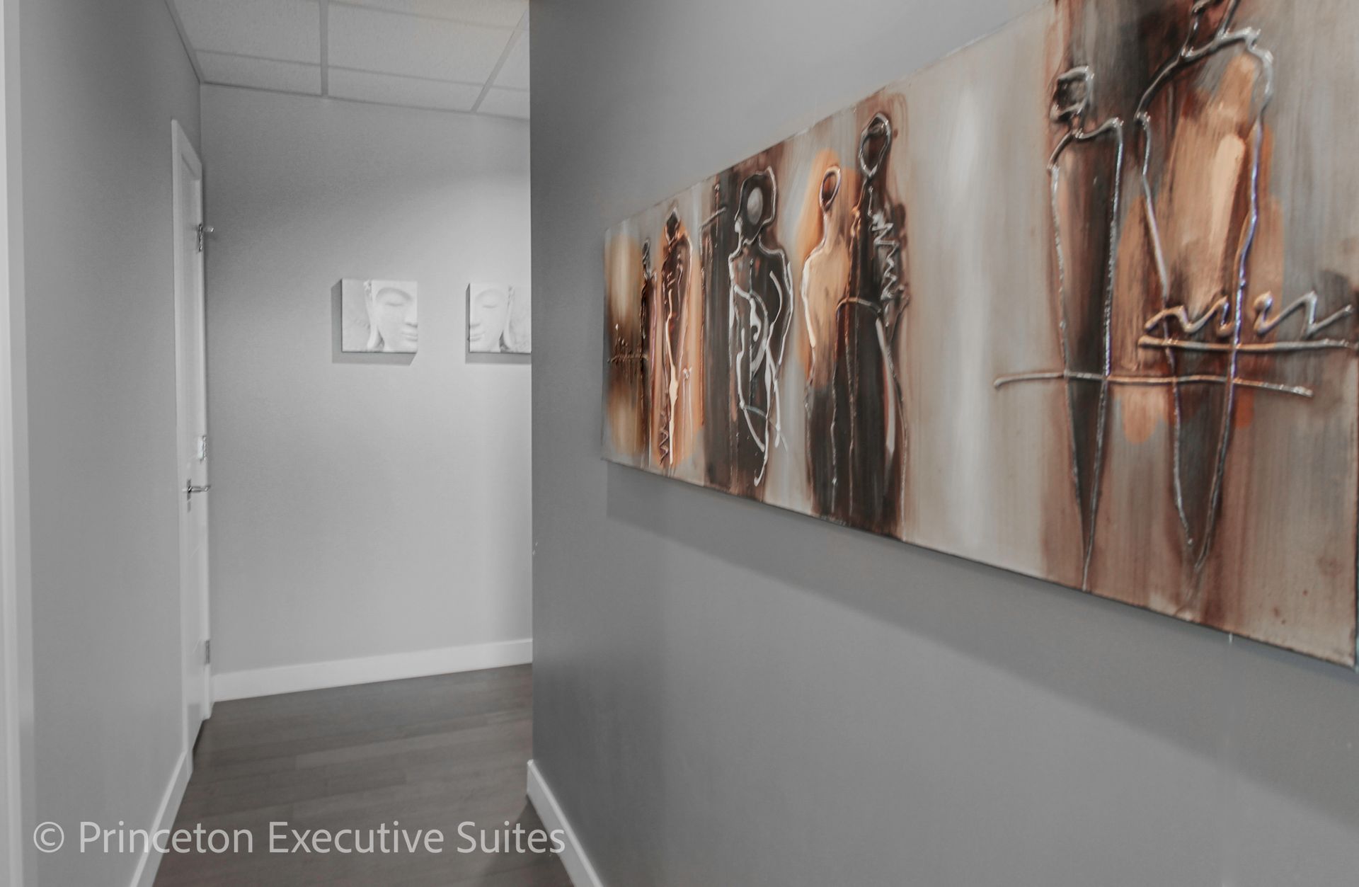 Hallway with art on the right, light gray walls, wood floor, and doors on the left.
