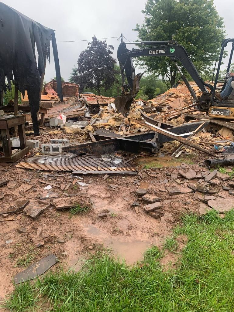 A house is being demolished by an excavator in a field.