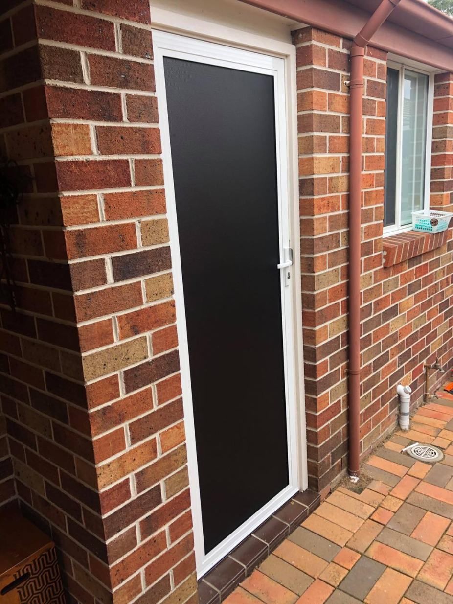 A Black Door Is On The Side Of A Brick Building — Central Coast Flyscreen Service In West Gosford, NSW