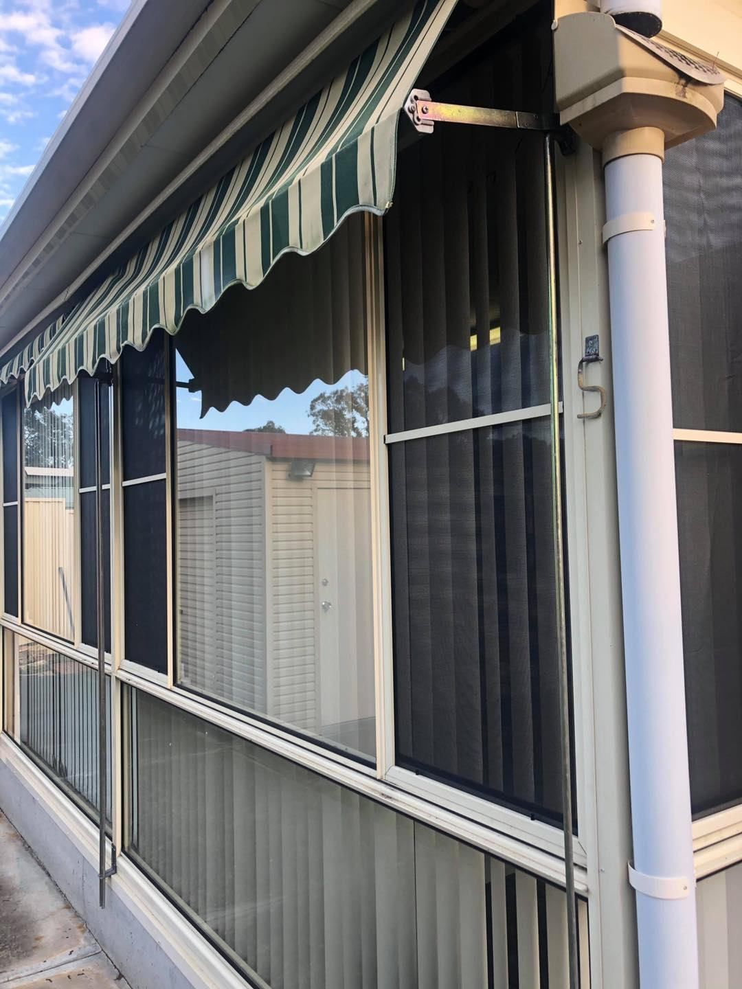 A House With A Striped Awning Over The Windows — Central Coast Flyscreen Service In West Gosford, NSW
