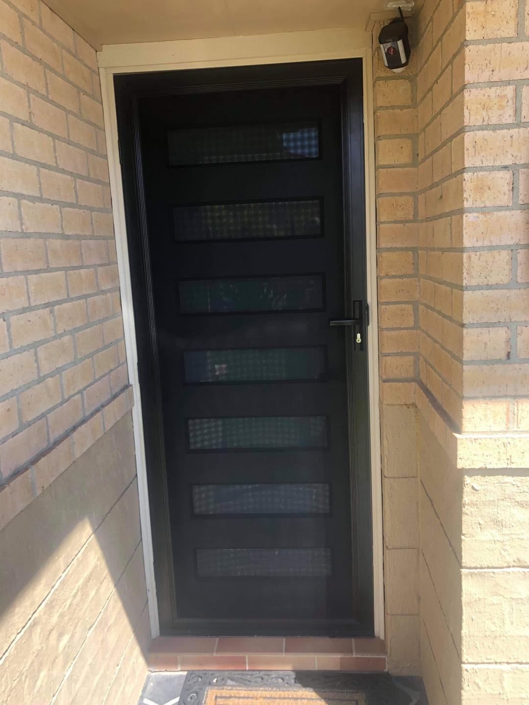 A Black Door Is On The Side Of A Brick Building — Central Coast Flyscreen Service In Warnervale, NSW
