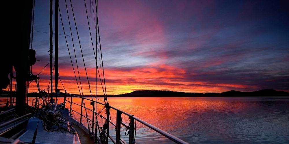 A Sailboat Is Floating On Top Of A Body Of Water At Sunset — Central Coast Flyscreen Service In West Gosford, NSW