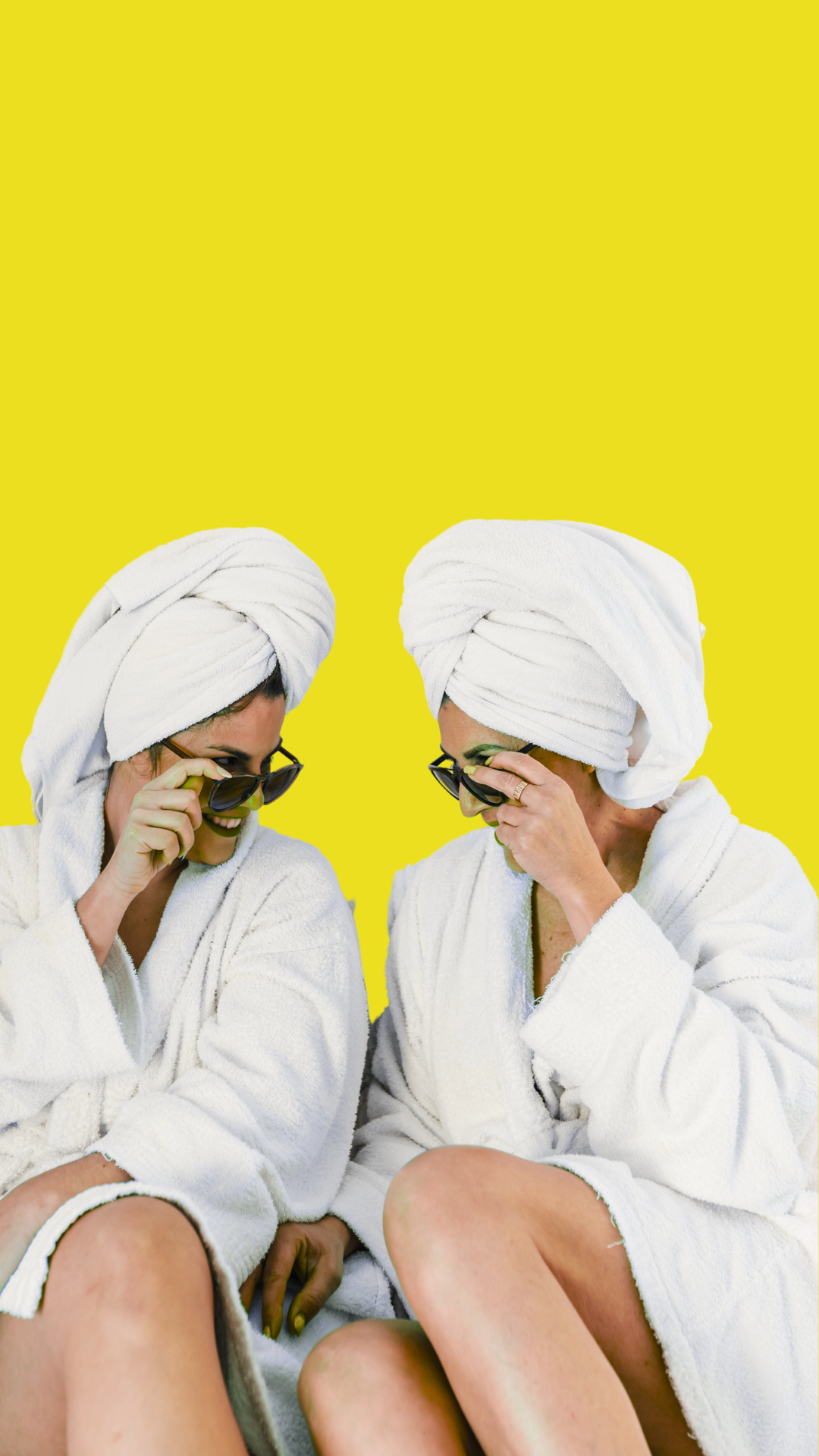 Two women in bathrobes with towels wrapped around their heads are sitting next to each other.