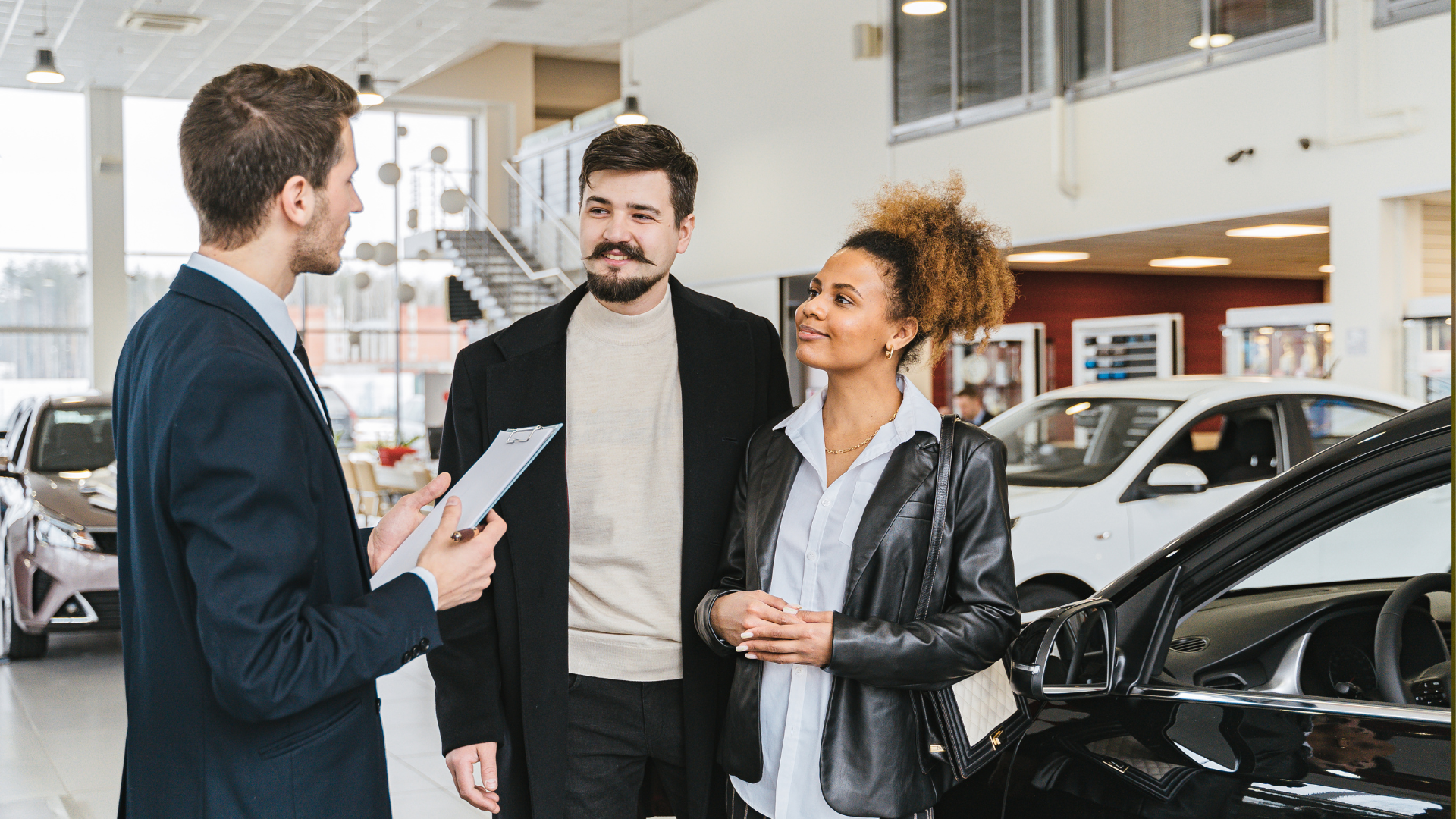 A man is talking to a woman and a man in a car showroom.